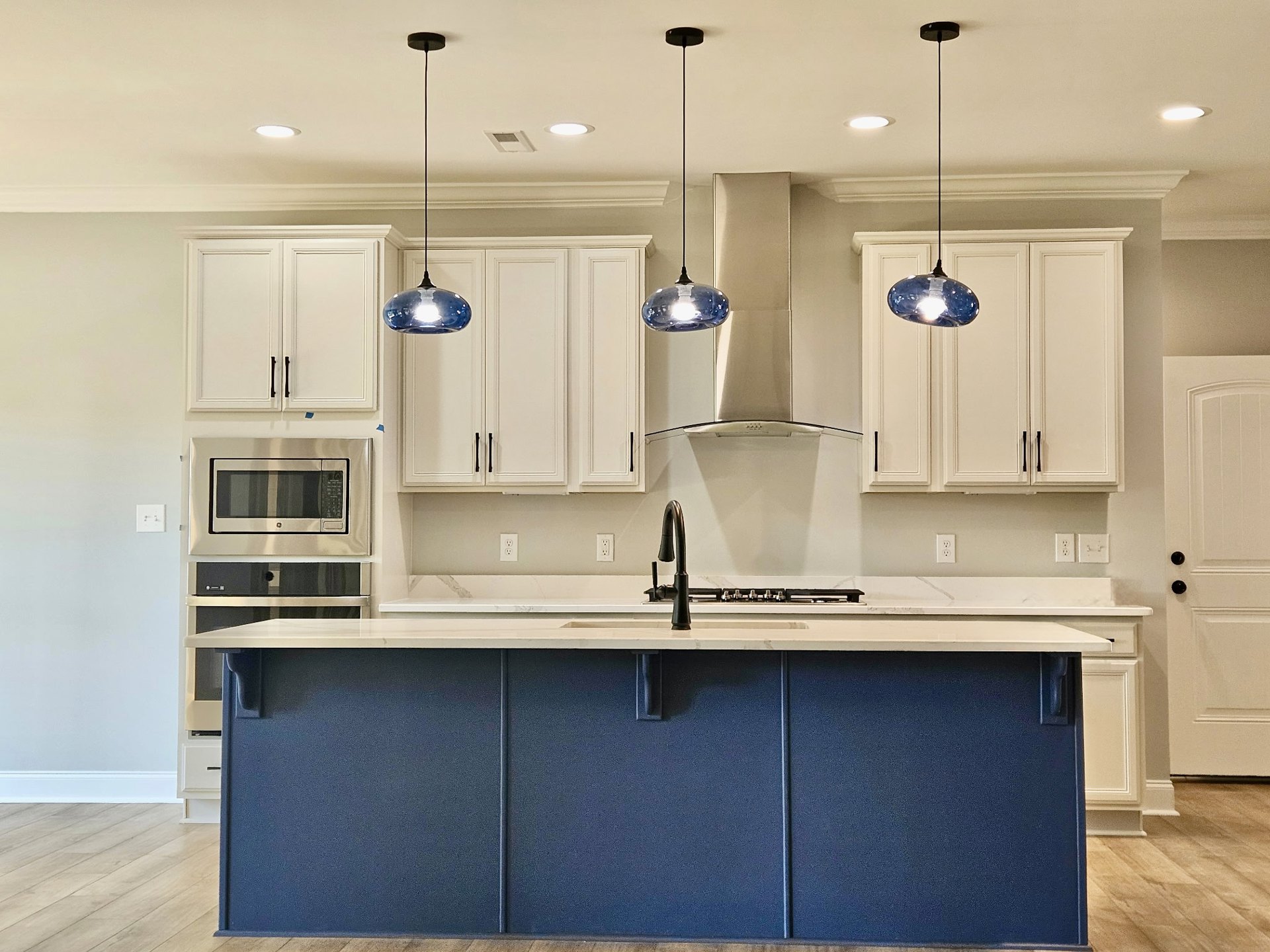 Open kitchen with blue island countertop, built-in stove, white walls, black trim, white ceiling with crown molding, modern cabinetry, stainless steel microwave, hardwood flooring