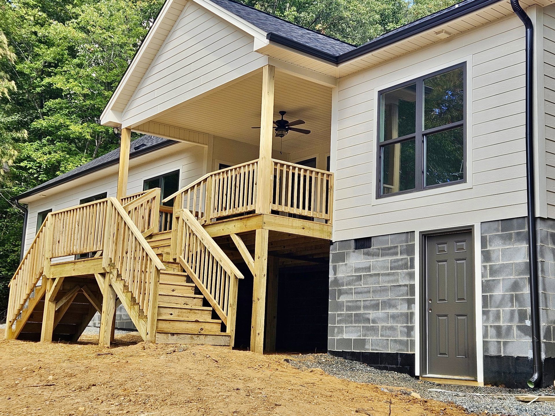 White siding house with wooden porch and stairs, grey front door, large window reflecting trees, ceiling fan with light fixture above porch