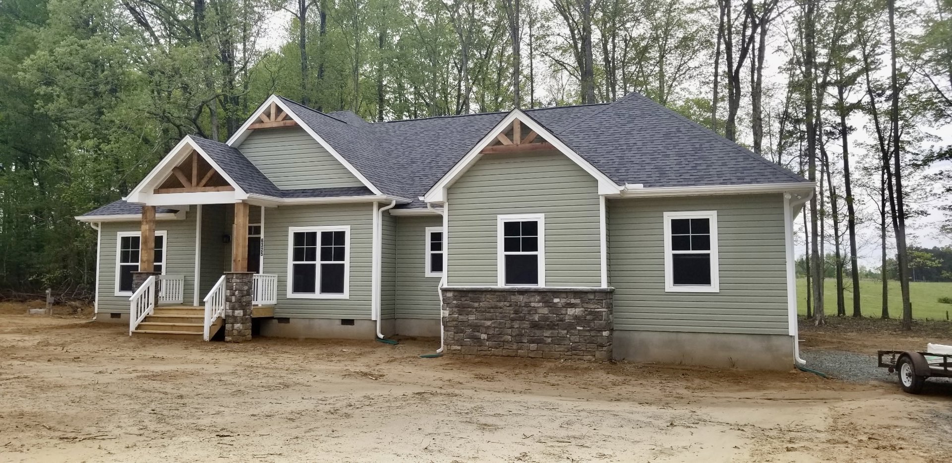 Brick house with multi-pane white-framed windows, dirt road leading to entrance, surrounded by mature trees