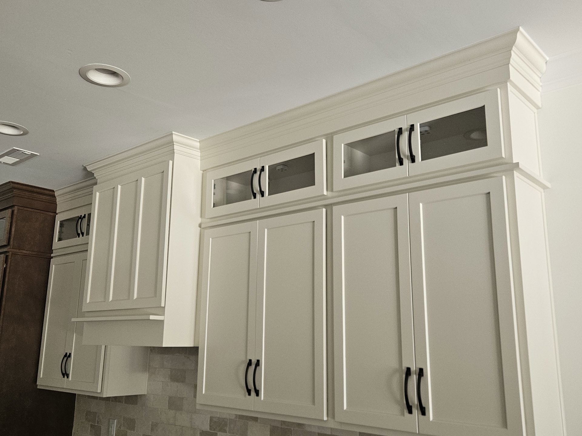 White kitchen cabinets with black handles, white ceiling light fixture, brown countertop, close-up of cabinet door and handle, plaster walls with molding