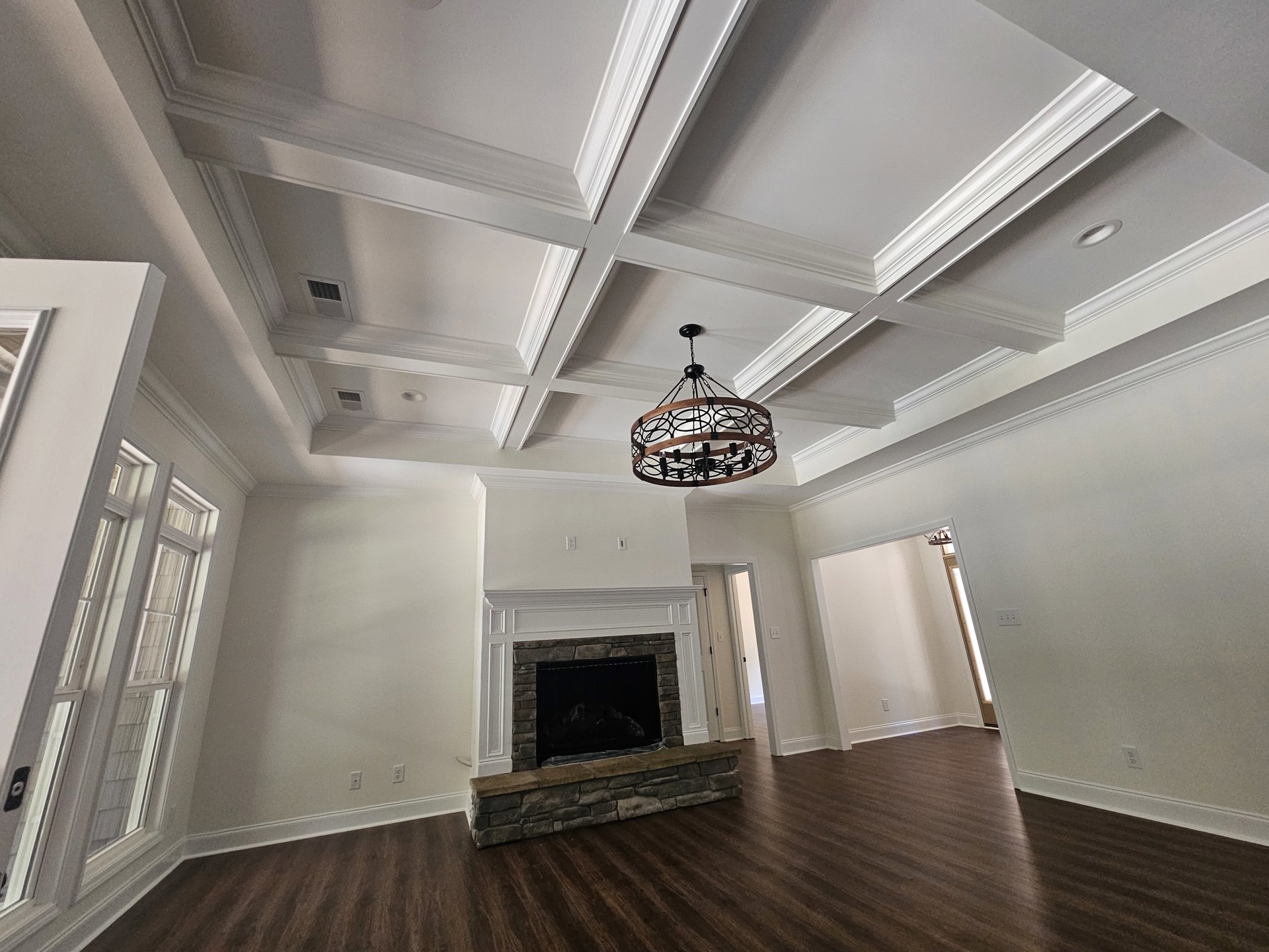 Living room with stone fireplace, white mantel, wood flooring, and chandelier featuring a wood ring and black metal frame