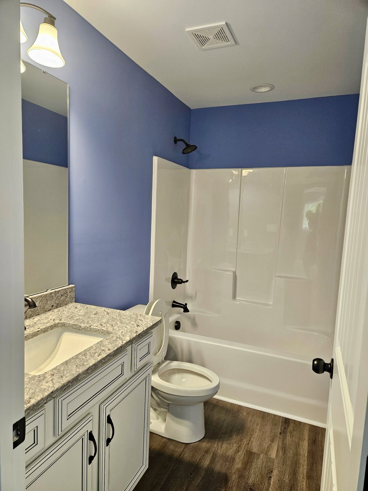 White triangular sink and chrome faucet beside a modern toilet, gray tile flooring, vent in ceiling, black door knob on white wall