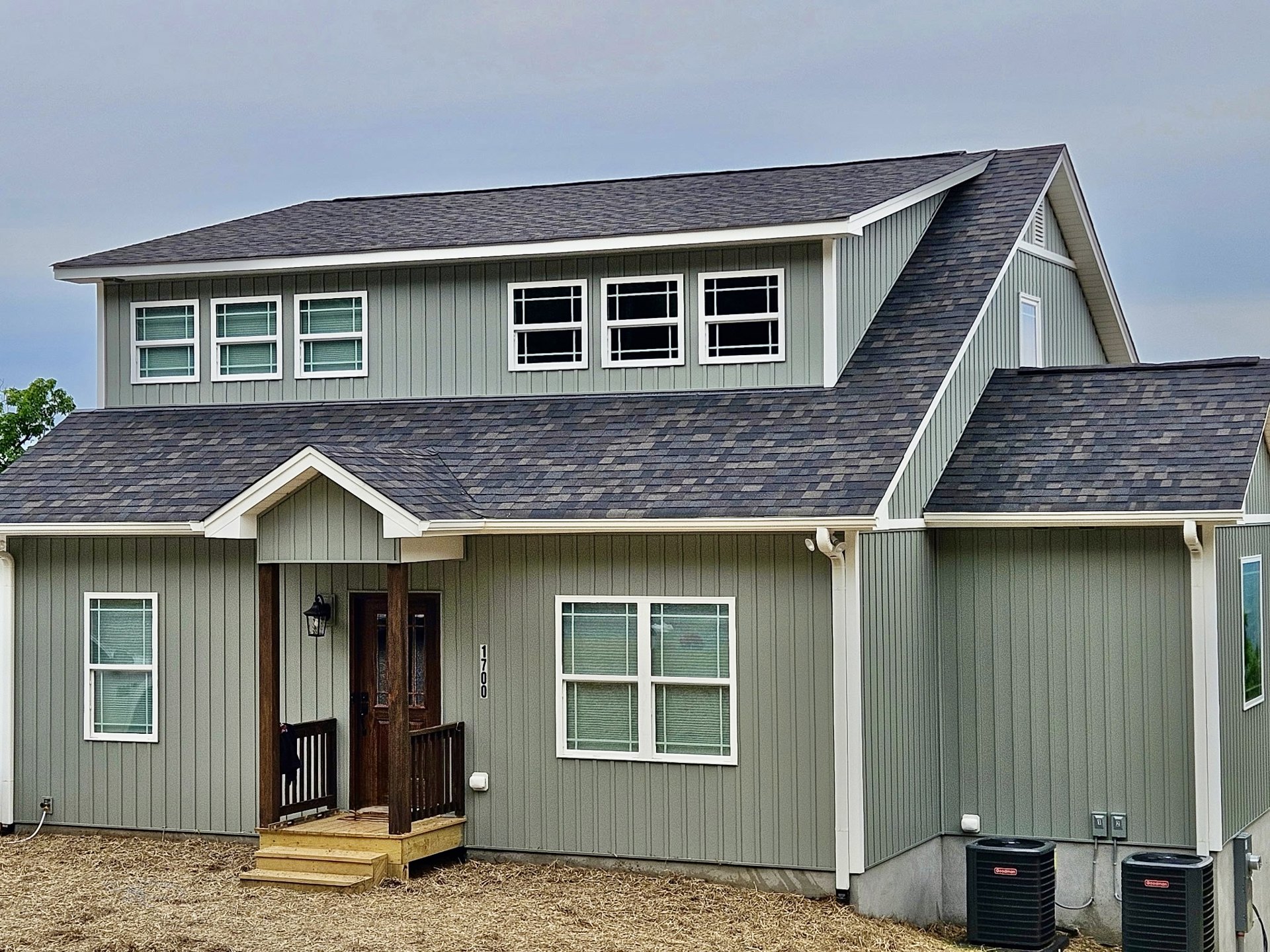 White cottage-style home with horizontal siding, covered front porch, white framed windows with blinds, dark front door, and gabled roof against blue sky