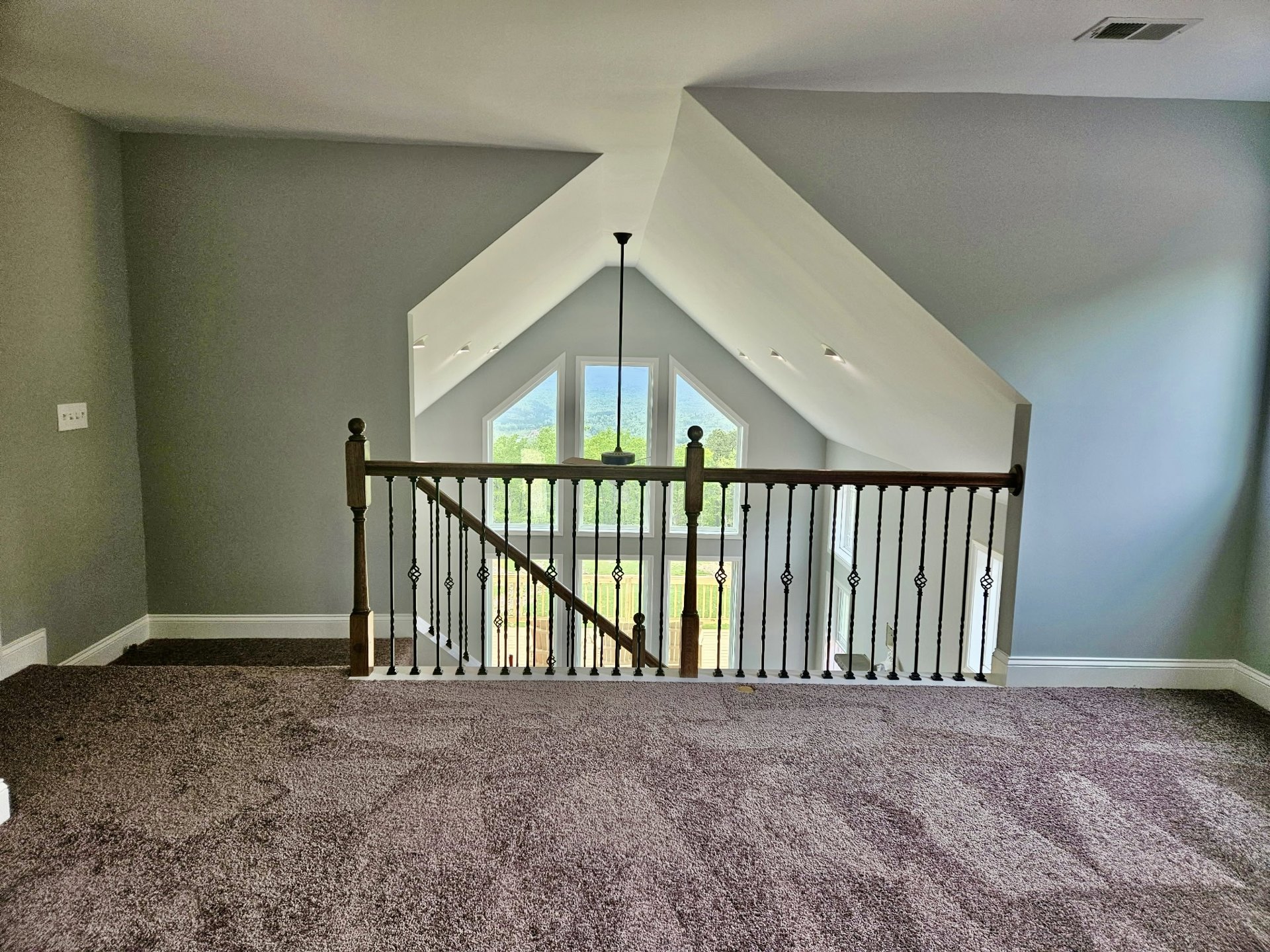Open living area with carpeted floor, white walls, staircase with wooden handrail, large window and glass balcony door, table lamp, natural light illuminating space
