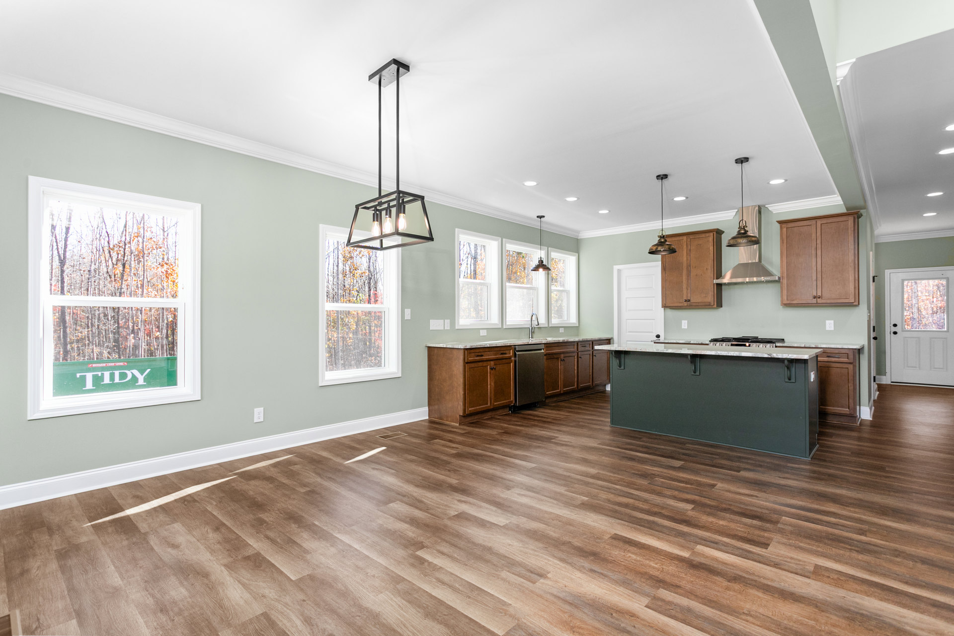 Open kitchen and dining area with hardwood floors, wooden cabinetry with knobs, kitchen counter featuring a stove, white door with window, large window overlooking trees, black