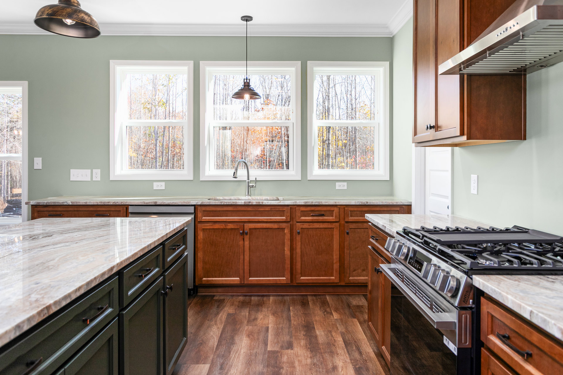 Kitchen featuring wood cabinets, marble countertops, black lower cabinets, built-in stovetop with griddle, large window overlooking trees, and white surfaces with black accents