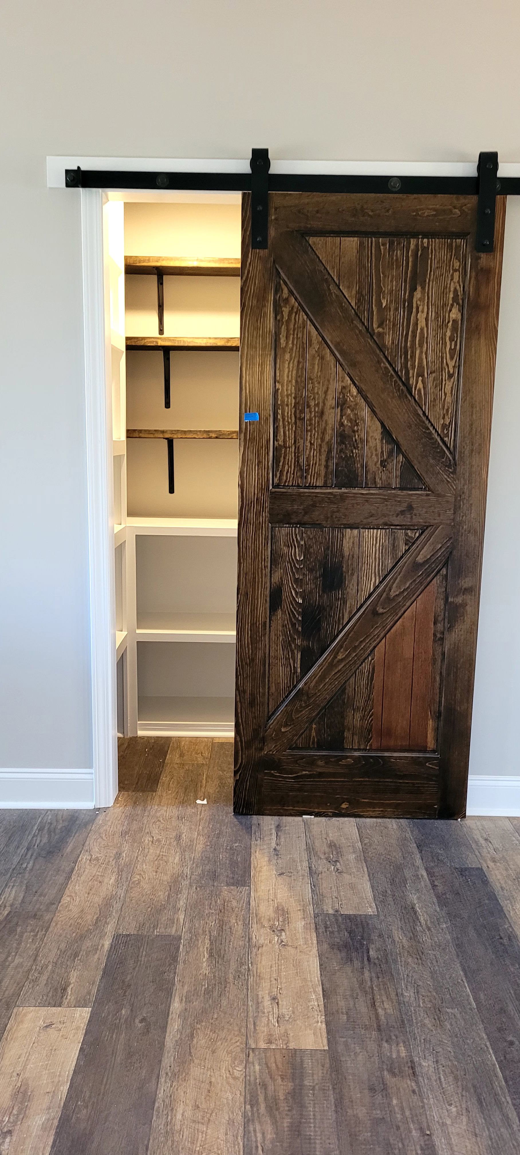 Closet with wooden door featuring blue tape, wood plank flooring, white shelving, and white walls with framed trim