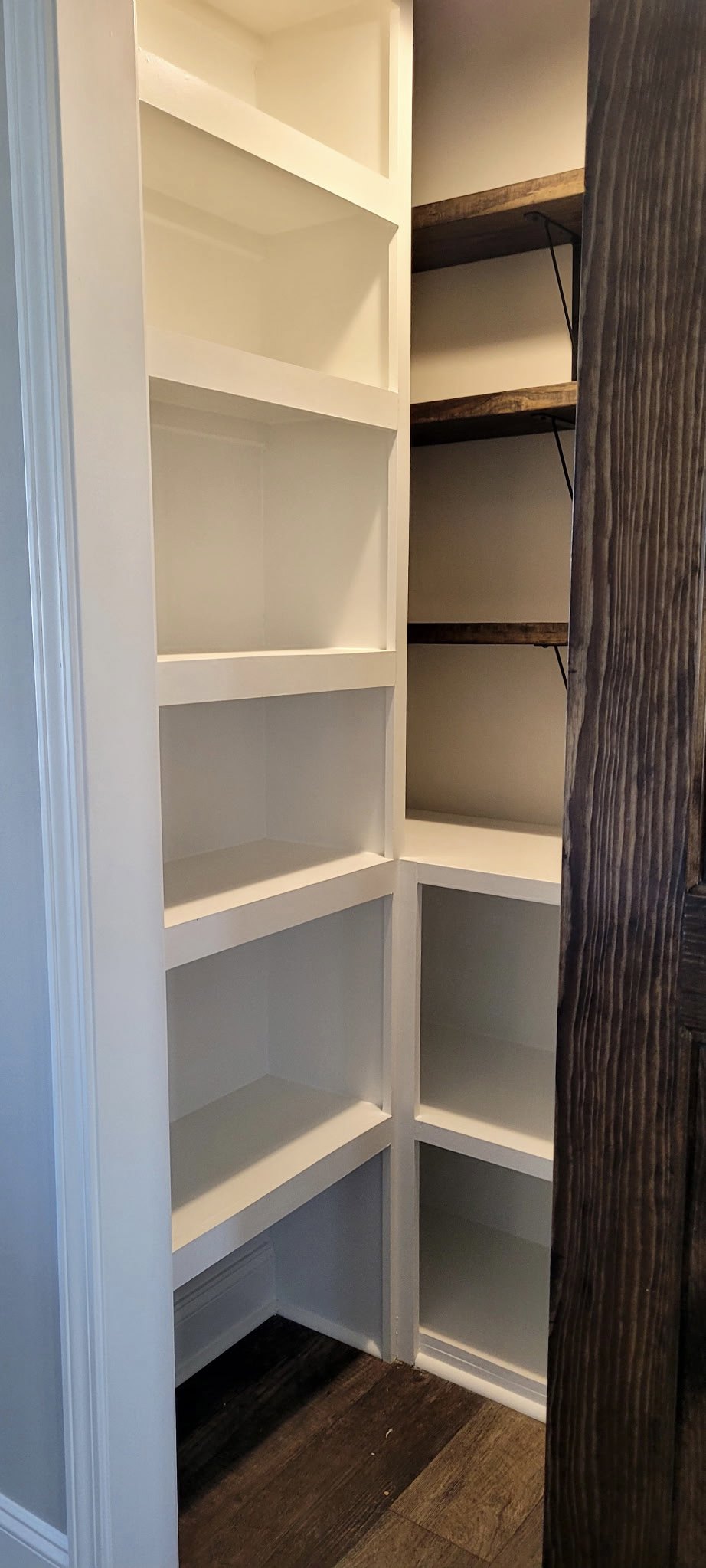 White built-in closet shelves with wood flooring, white door, and subtle shadows on the shelving surfaces.
