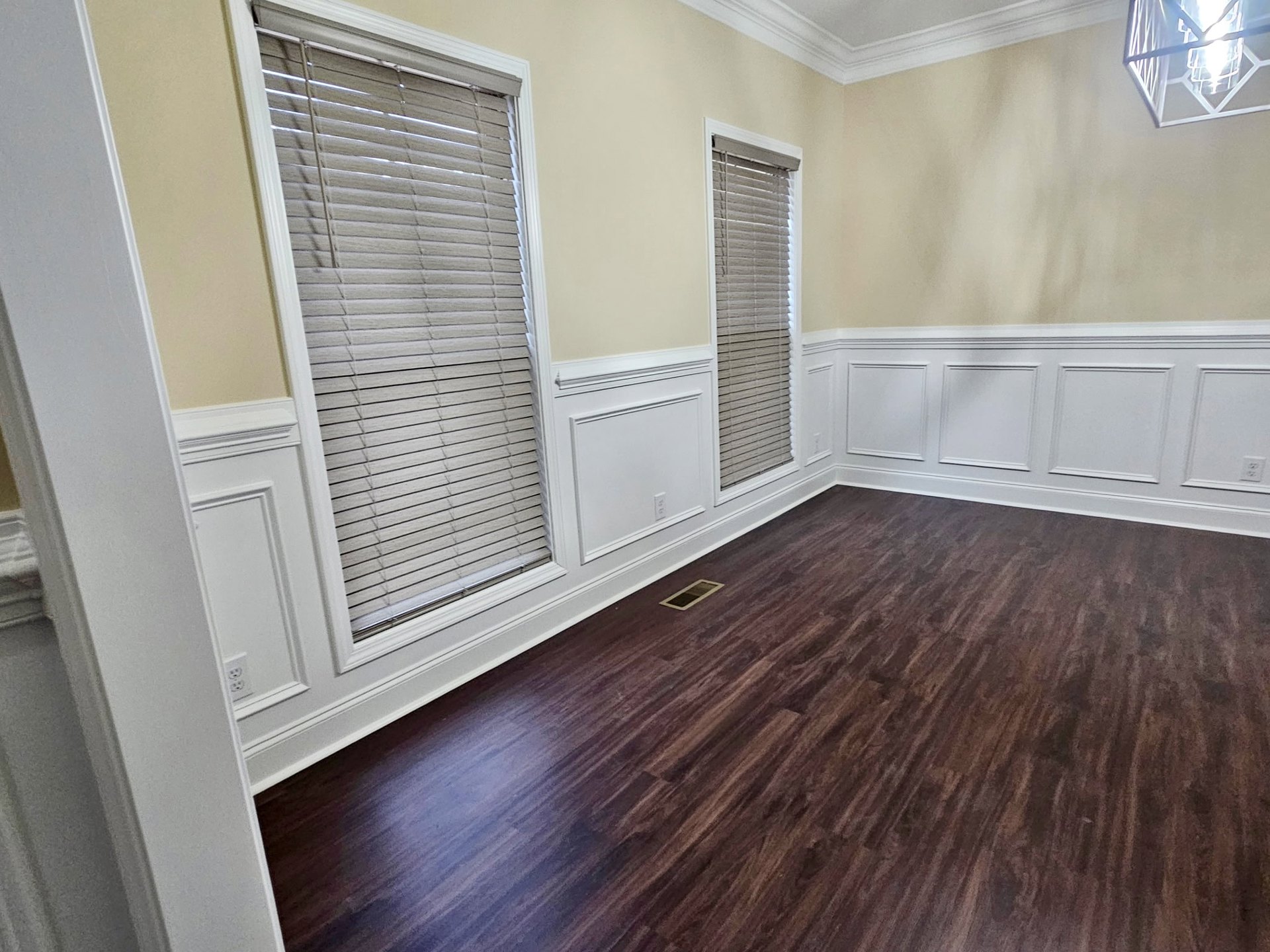 Wood floor with natural finish, white walls, wire frame ceiling light fixture, window with white blinds, white wall featuring a light switch, simple baseboard molding