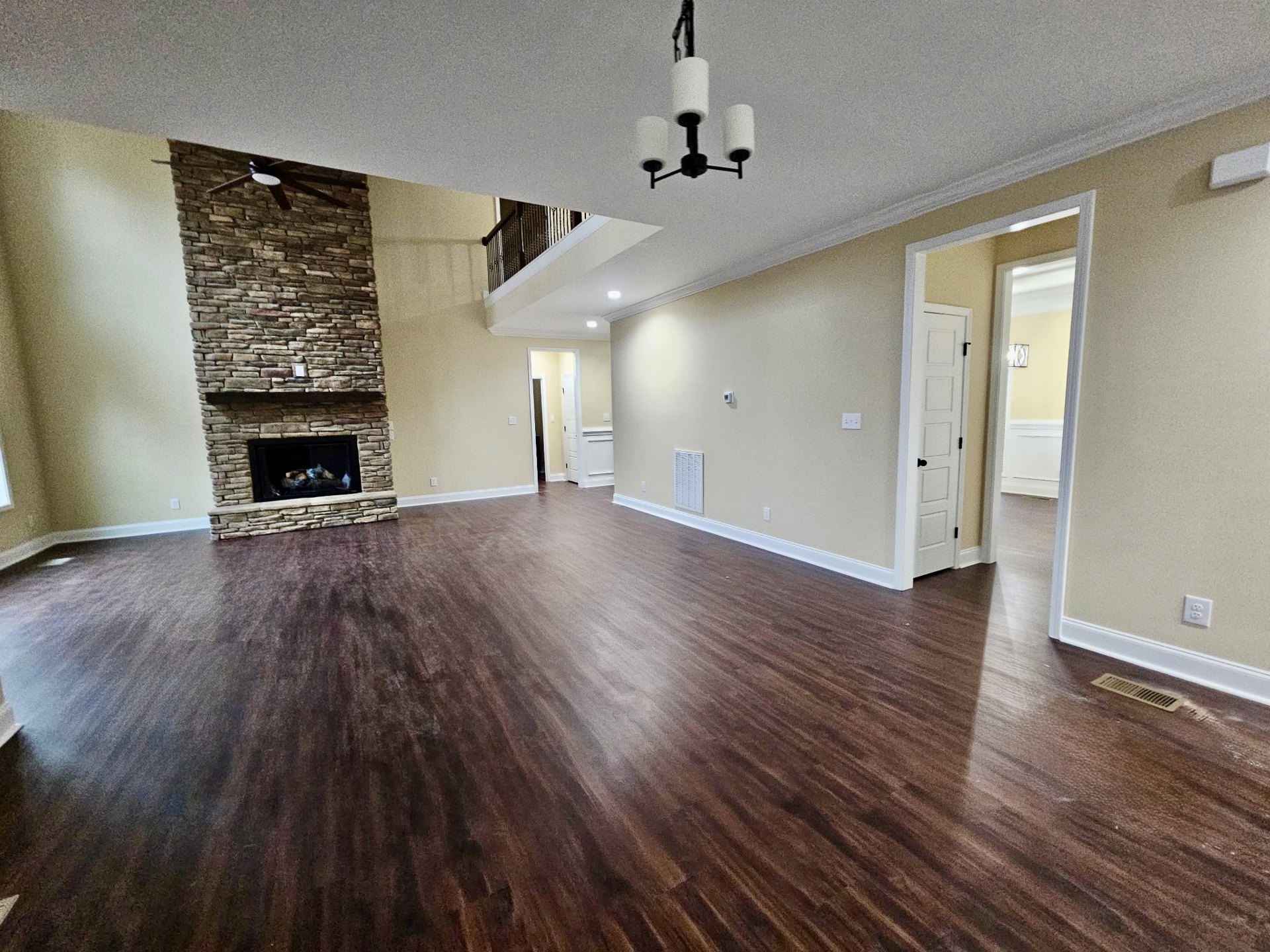 Spacious living room featuring hardwood floors, stone fireplace with stacked firewood, white door with black handle, and neutral walls.