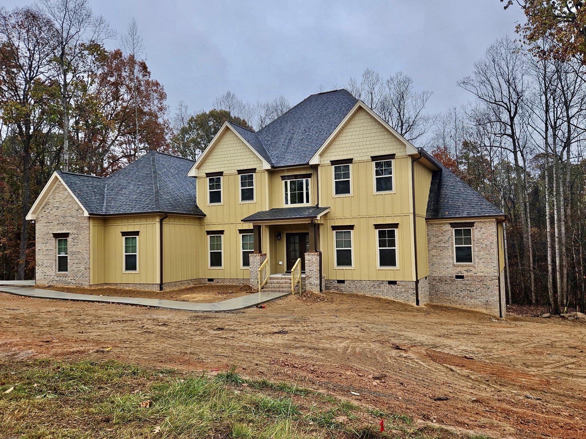 Yellow house with white-framed windows, covered porch, and dirt yard with a driveway; mature tree and blue sky in background.