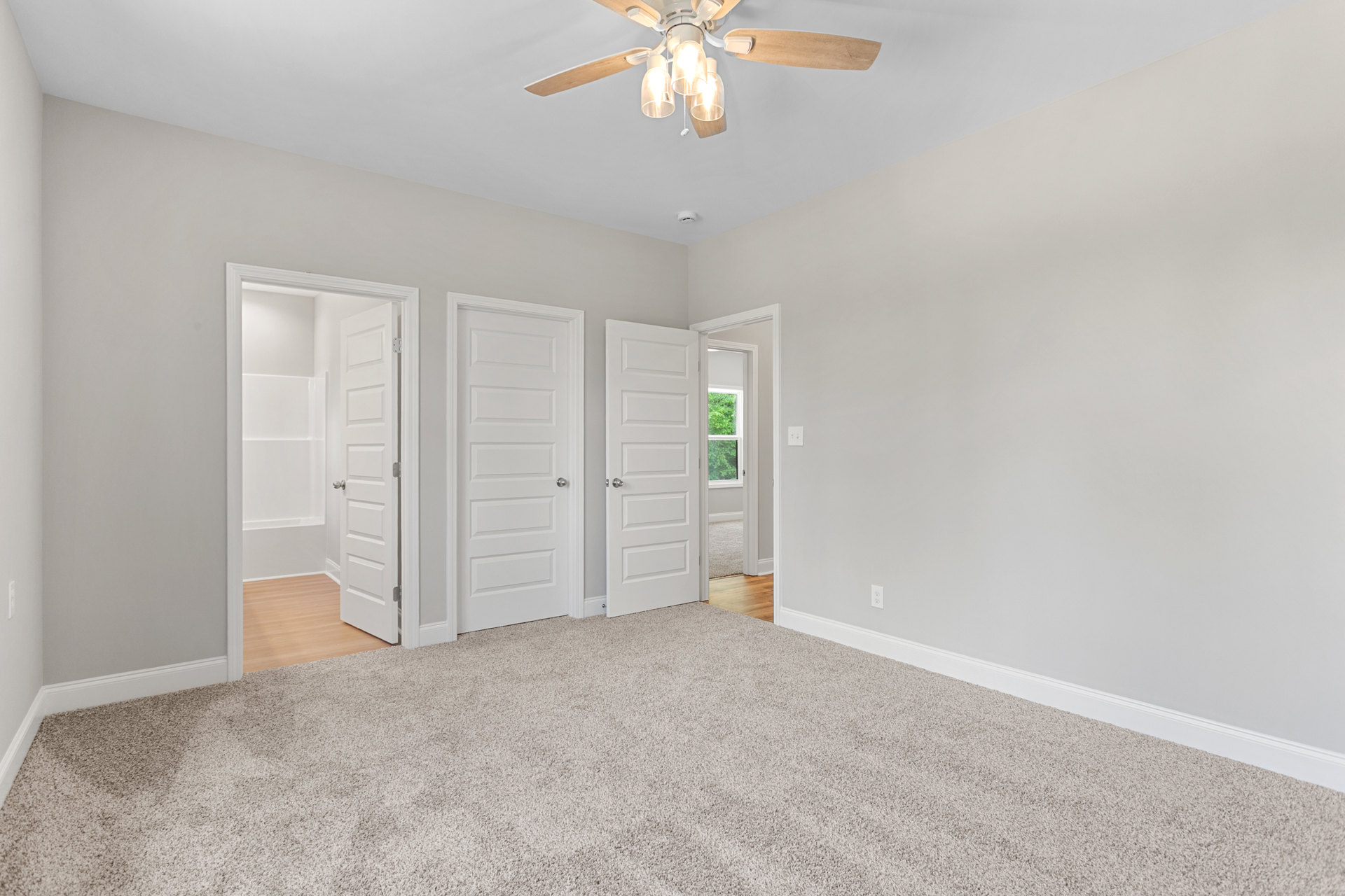 Carpeted room with four white doors, silver handles, ceiling fan with lights, and open door revealing white bathroom