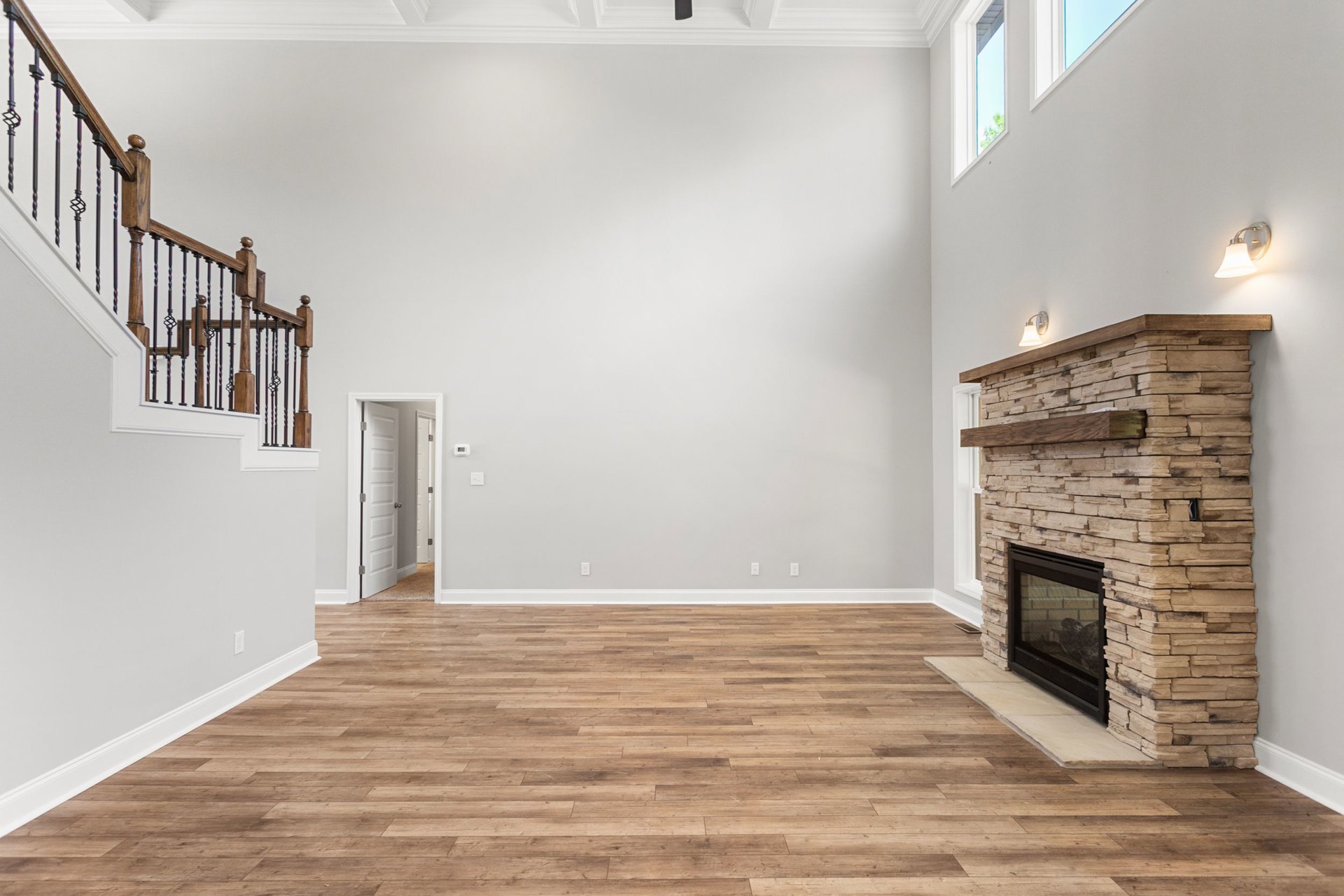 Living room with hardwood flooring, white walls, glass-door fireplace, wooden staircase with metal railings, and wall-mounted light fixture