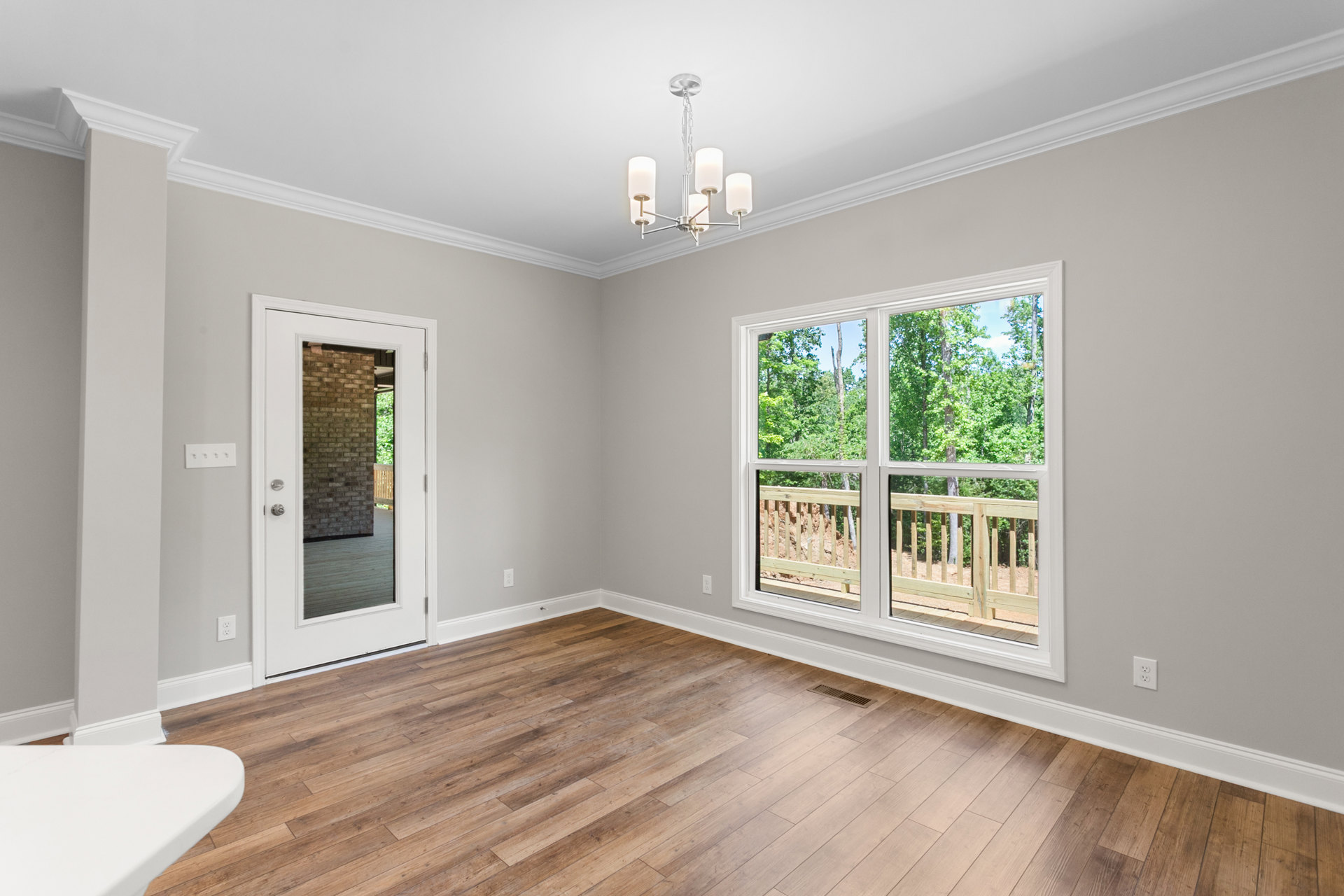 Wood-floored room with white table, mirrored door, two windows showing trees and wooden railing, wall vent in corner