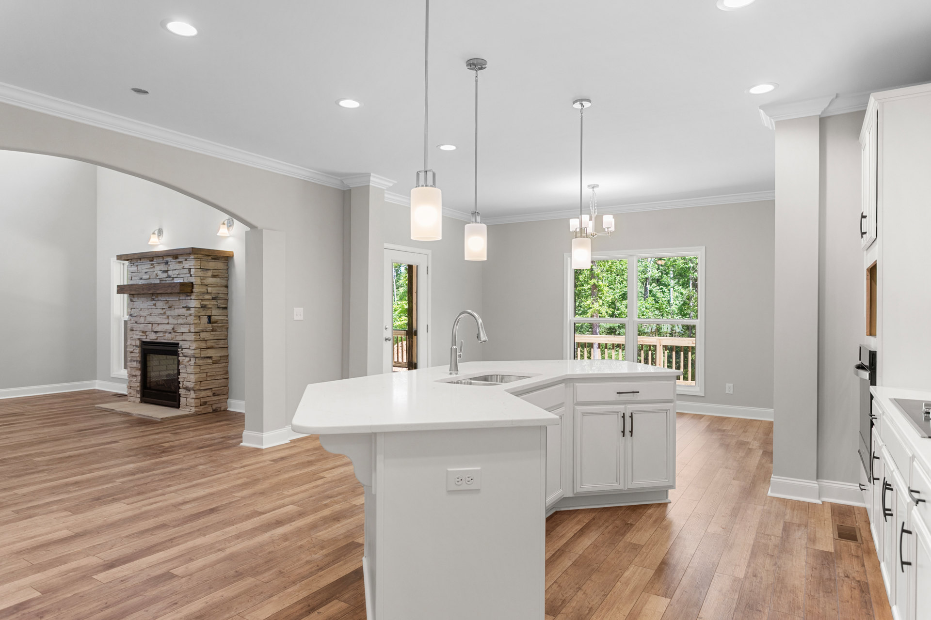 Open-concept kitchen and living room featuring a tiled fireplace with wood mantel, white kitchen island with double sinks, ceiling light fixture, cabinetry, and large window