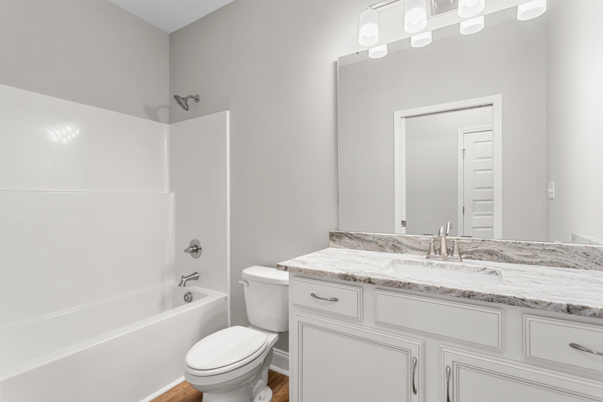 White bathtub with chrome showerhead, adjacent to closed white toilet, surrounded by light tile walls and floor, bathroom fixtures visible