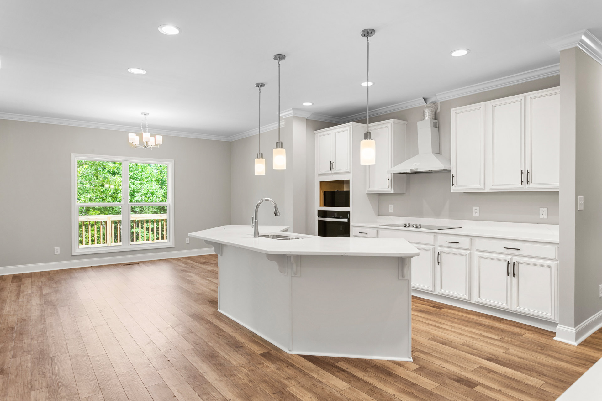 White kitchen with shaker cabinets, stainless steel sink and stove, wood plank flooring, large window overlooking trees, round pendant light fixture