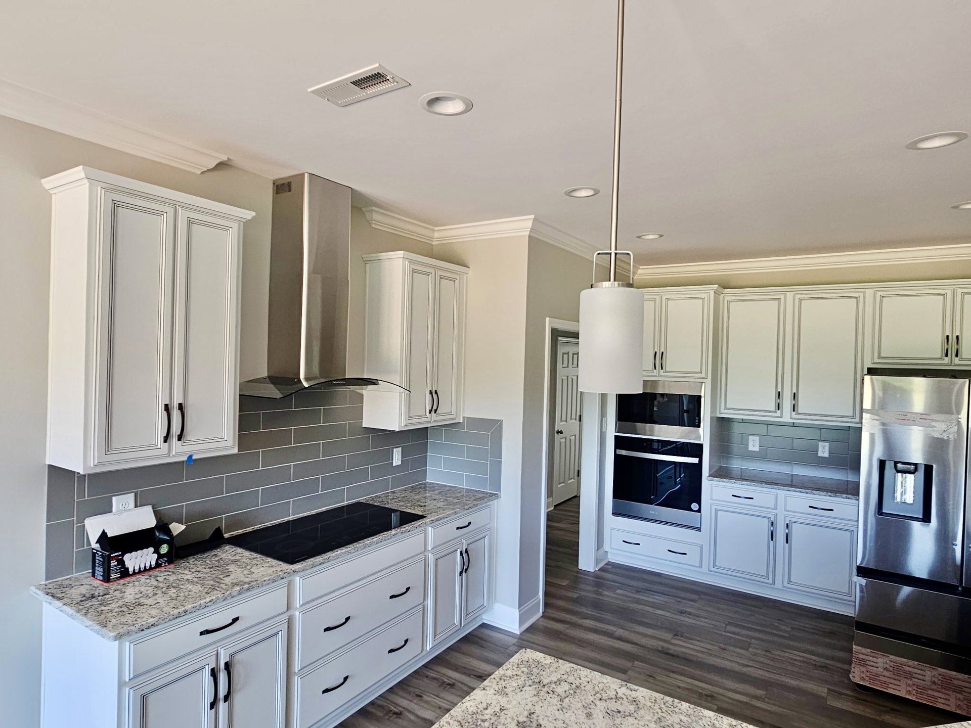 White kitchen cabinets with black handles, tile flooring, black countertop tiles, stainless steel oven, refrigerator, and white drawers, under recessed ceiling lighting.