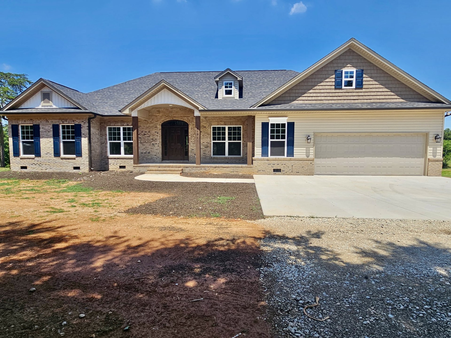 Two-story brick house with blue shuttered windows, white garage door with square panels, paved driveway, and covered front porch.