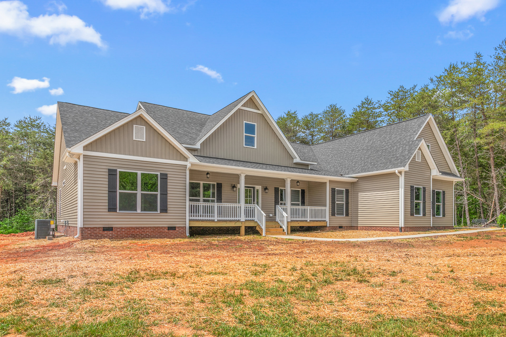 Two-story house with white porch railing, large windows, and wooden deck overlooking green lawn, mature trees, and Robert Frost Farm in the background
