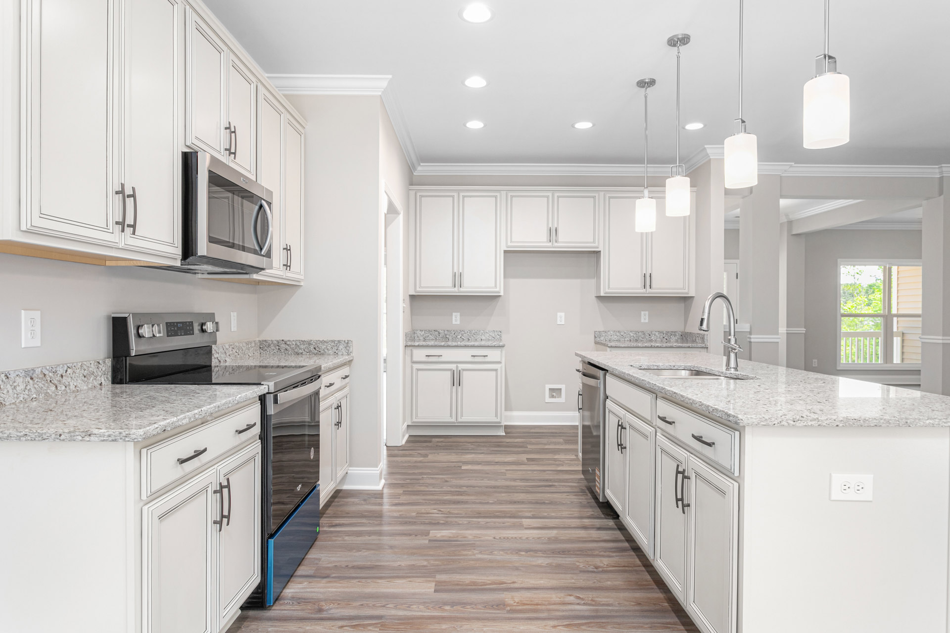 White kitchen cabinets, stainless steel stove and microwave, wood flooring, white-framed window, light-colored countertops