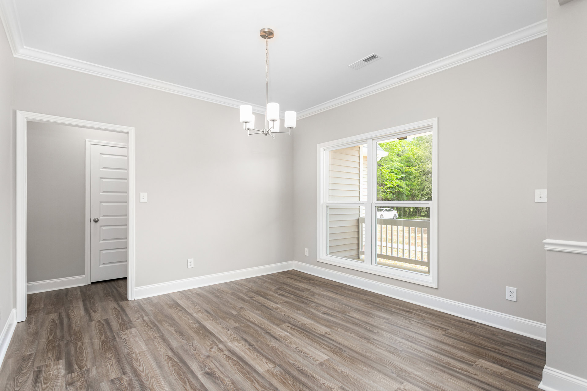 Wood flooring in a bright room with white walls, a white door with silver hardware, a window overlooking trees, and a modern lamp.