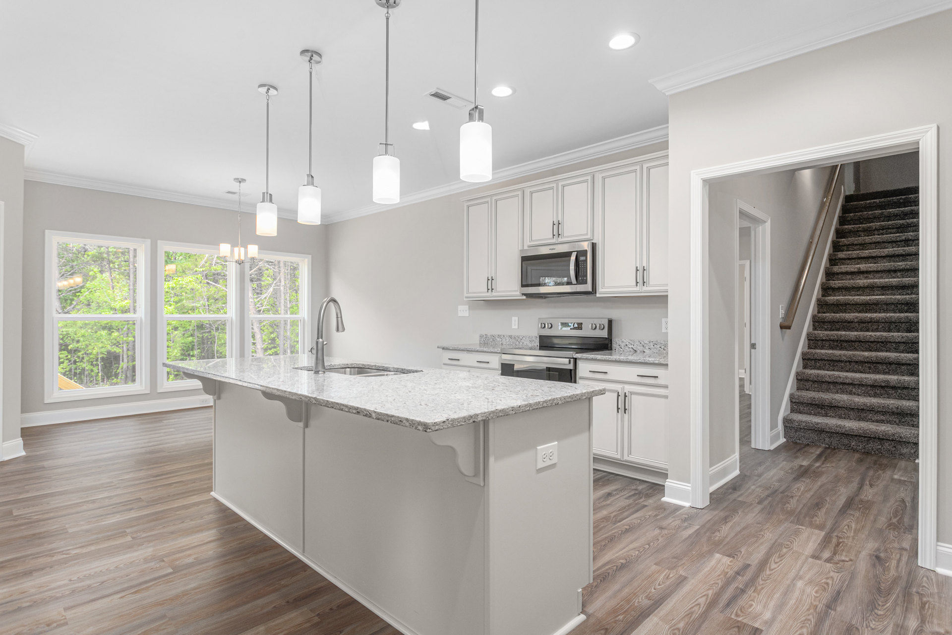 Kitchen with wood flooring, white countertops, open microwave, stainless steel pole, white cabinetry, and partial view of staircase