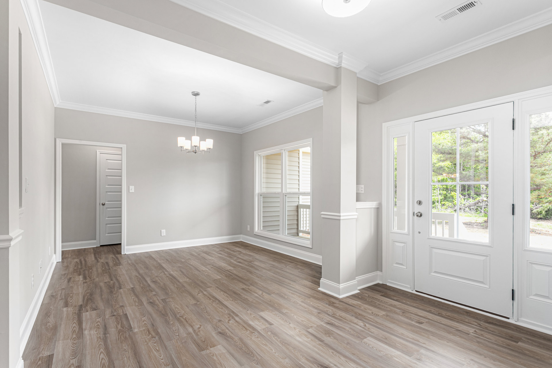 White walls, wood flooring, white doors with silver doorknobs, chandelier, window with glass panes, decorative molding