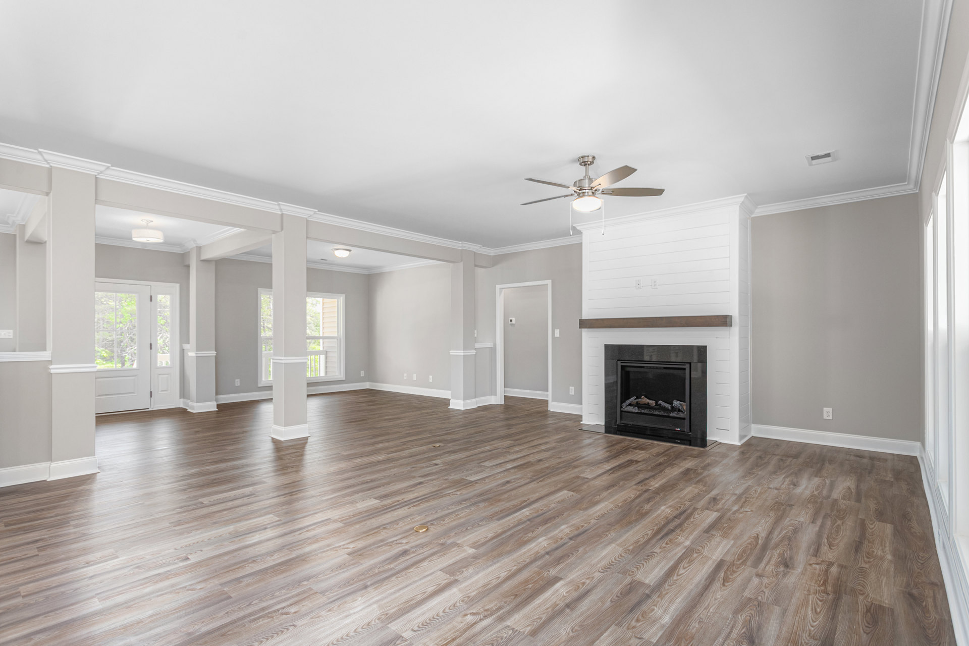 Spacious living room featuring hardwood floors, a wood-burning fireplace with stone surround, ceiling fan with light fixture, and a white door with glass panes.