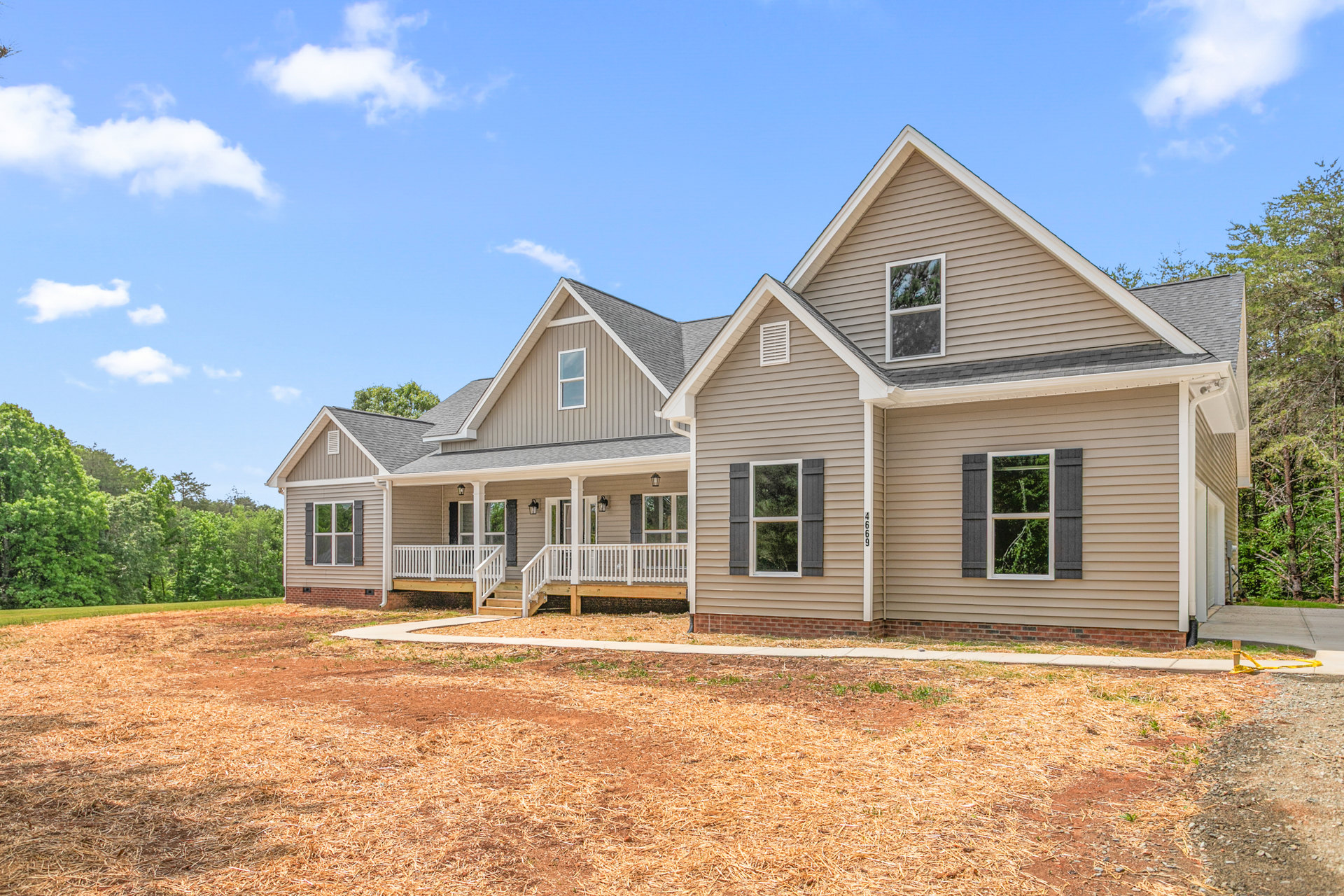 Two-story cottage with white siding, shuttered windows, and covered porch overlooking grassy yard bordered by mature trees; Robert Frost Farm visible in the background.