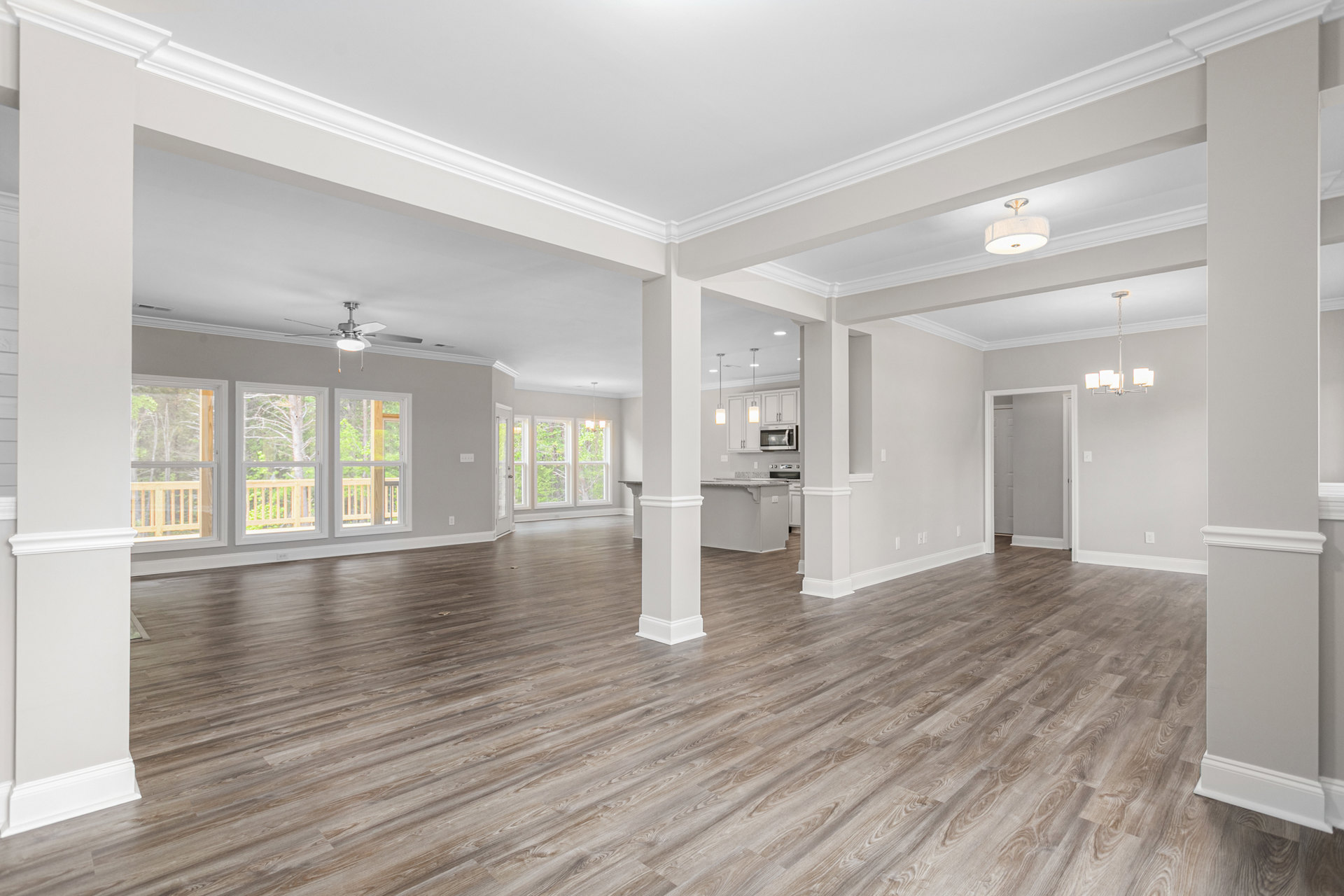 Spacious room with wood flooring, white pillars, ceiling fan, recessed lighting, large window overlooking trees, and white door with black handle