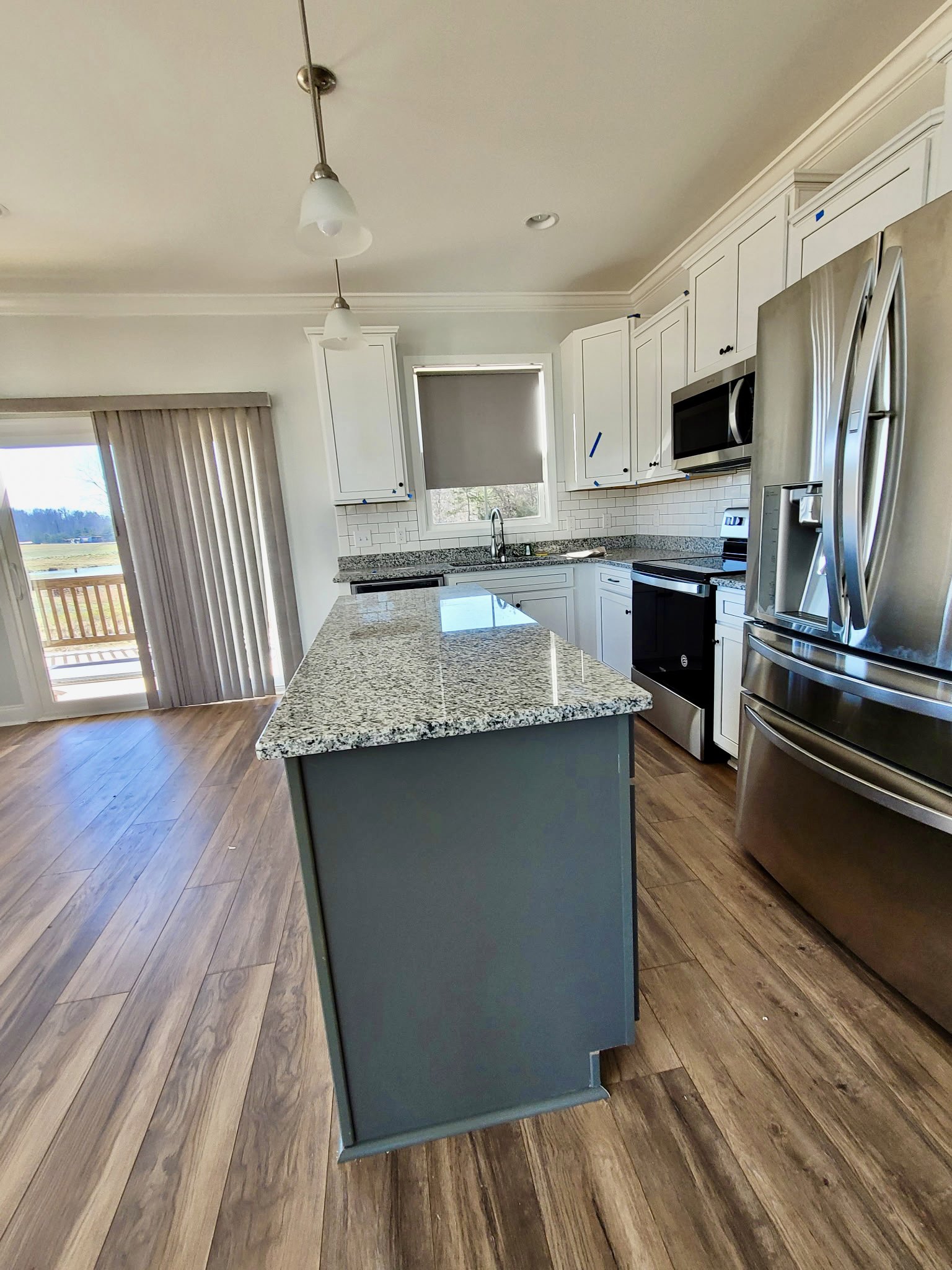 Granite island with undermount sink, stainless steel refrigerator, microwave, and oven, white cabinetry, tile flooring, sliding glass door, neutral walls