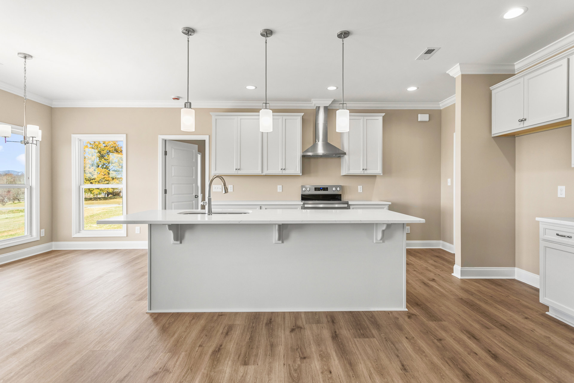 Kitchen with hardwood flooring, white cabinetry, stainless steel oven and stove, white countertop, window overlooking trees, modern central light fixture