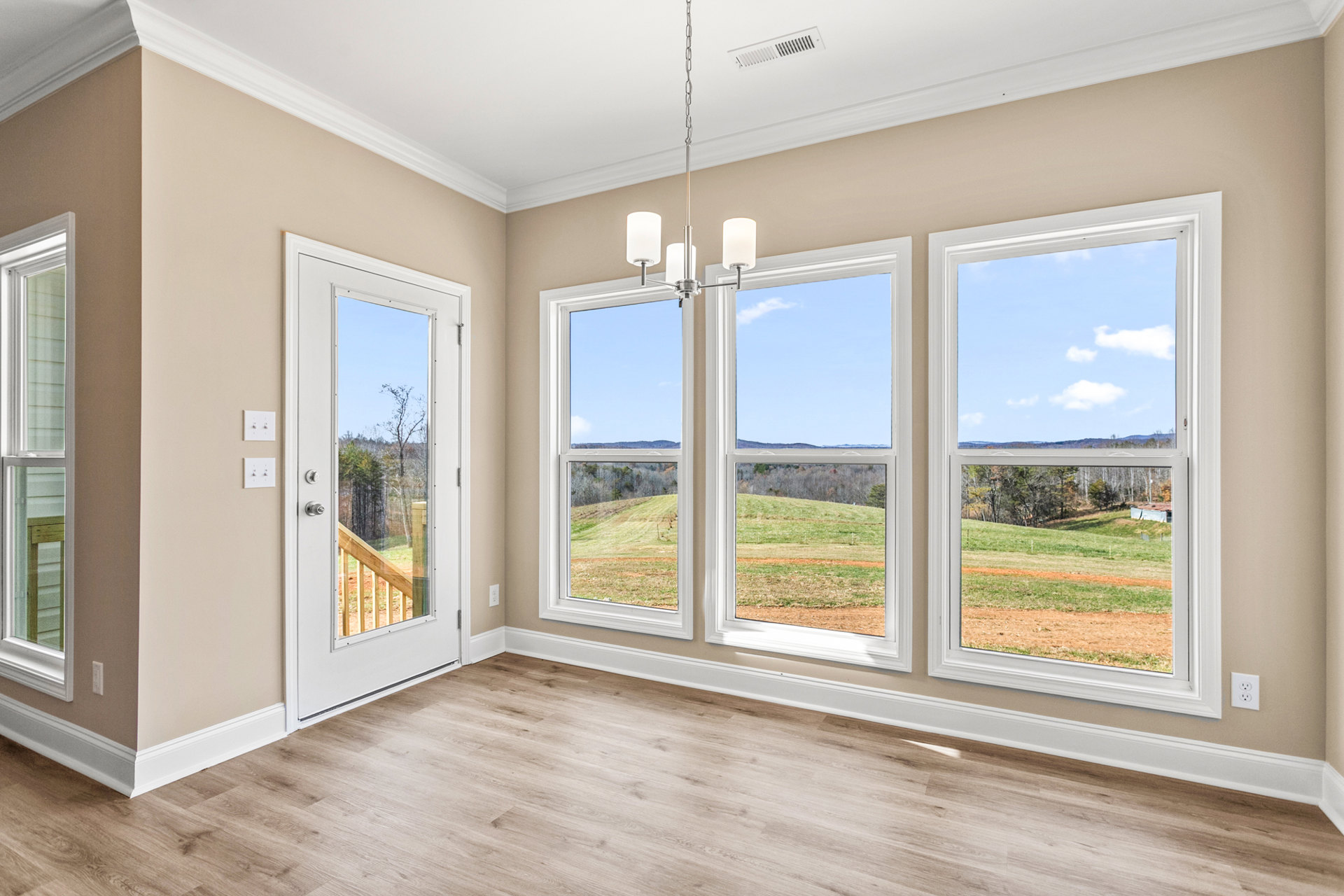 Wood-floored room with white trim, large windows and glass door opening to balcony overlooking grassy field and trees
