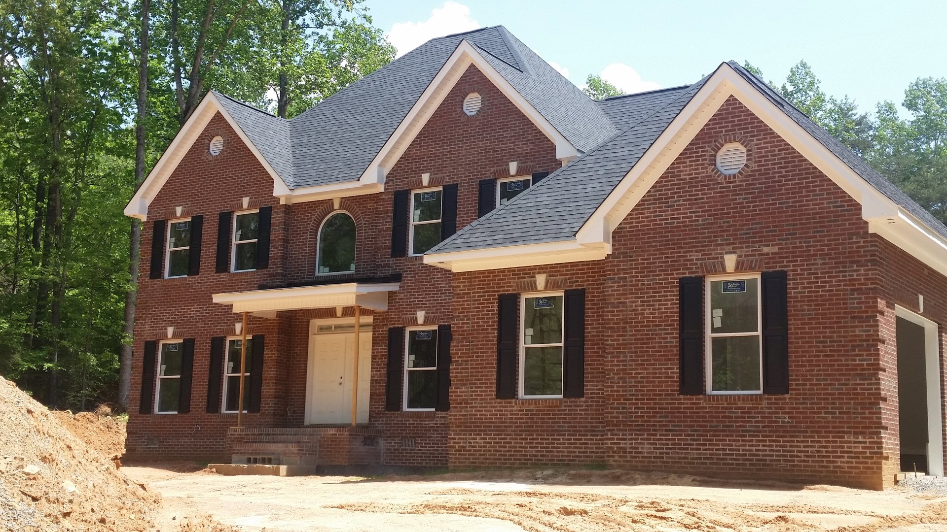 Red brick house with black shingle roof, white front door featuring a window, arched brick entryway with white trim, vent set into brick wall, large window with a note attached