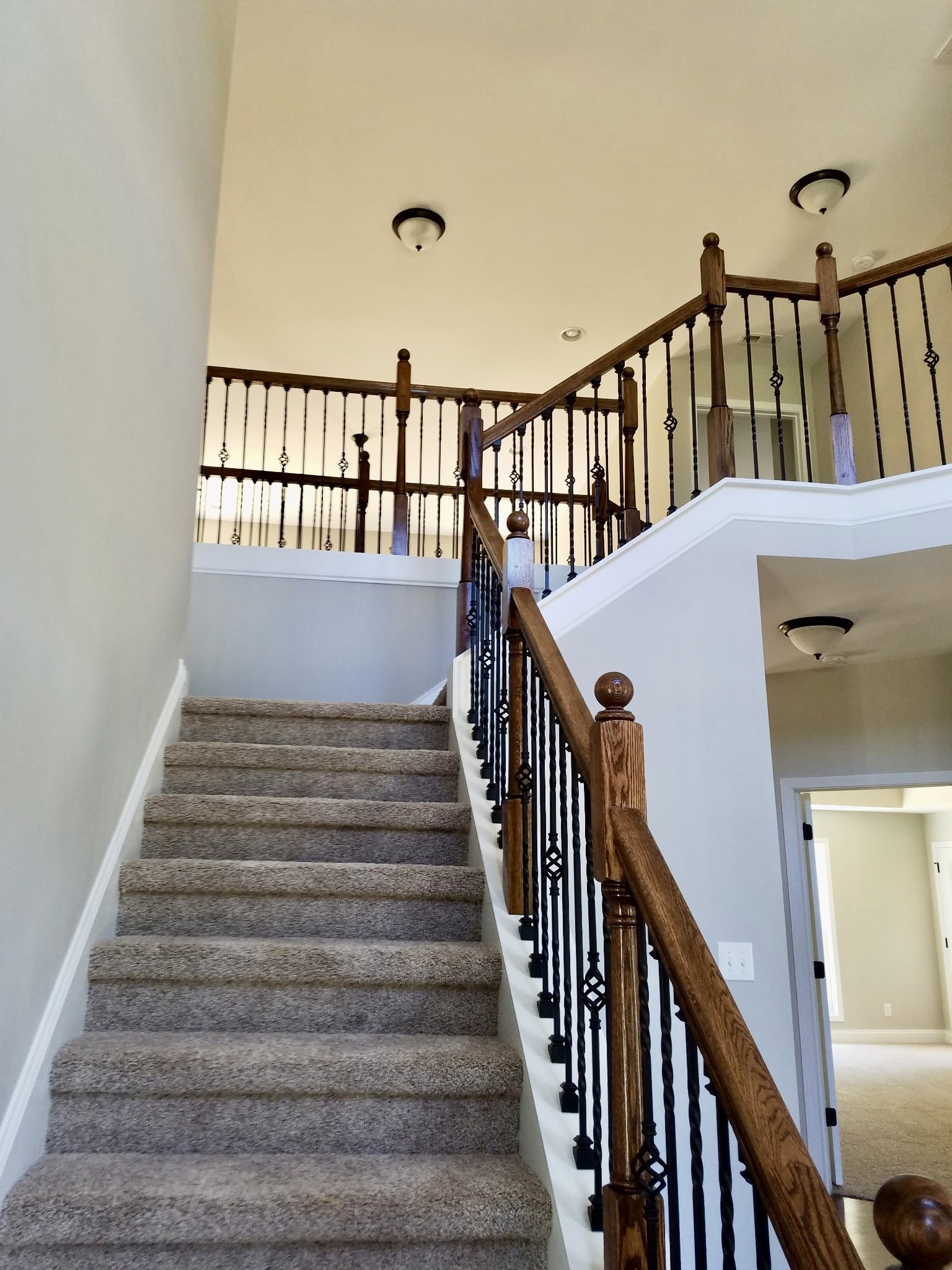 Carpeted staircase with wooden handrail and white balusters, light fixture mounted on ceiling, neutral painted walls