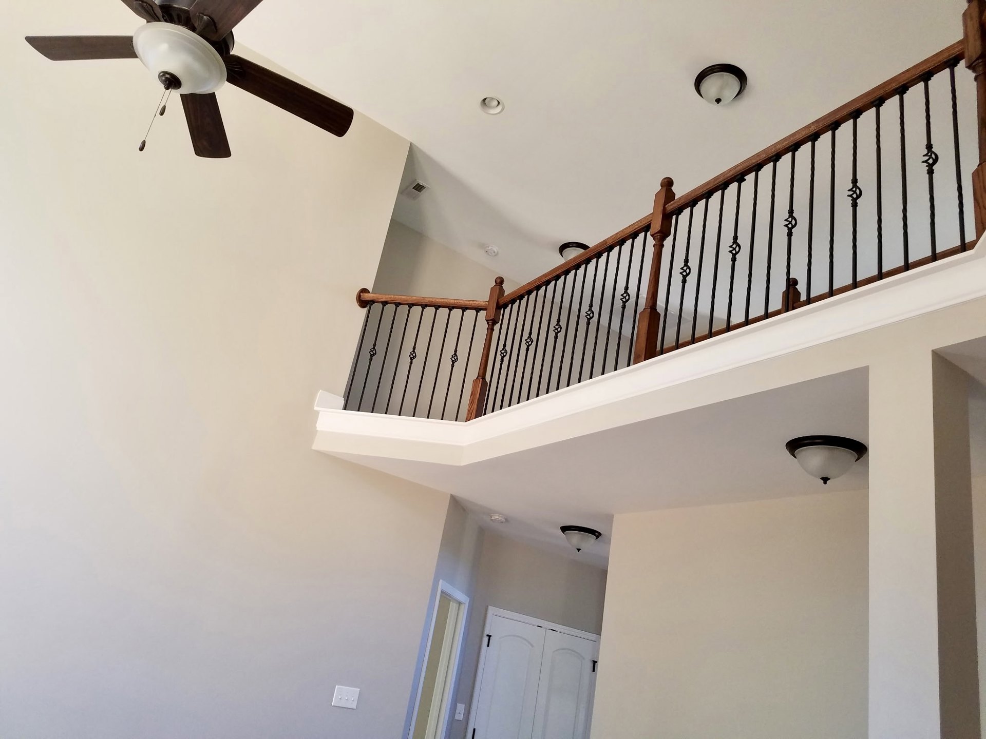 Ceiling fan with light fixture above a staircase featuring black metal railing, white walls, and a white door with black handles
