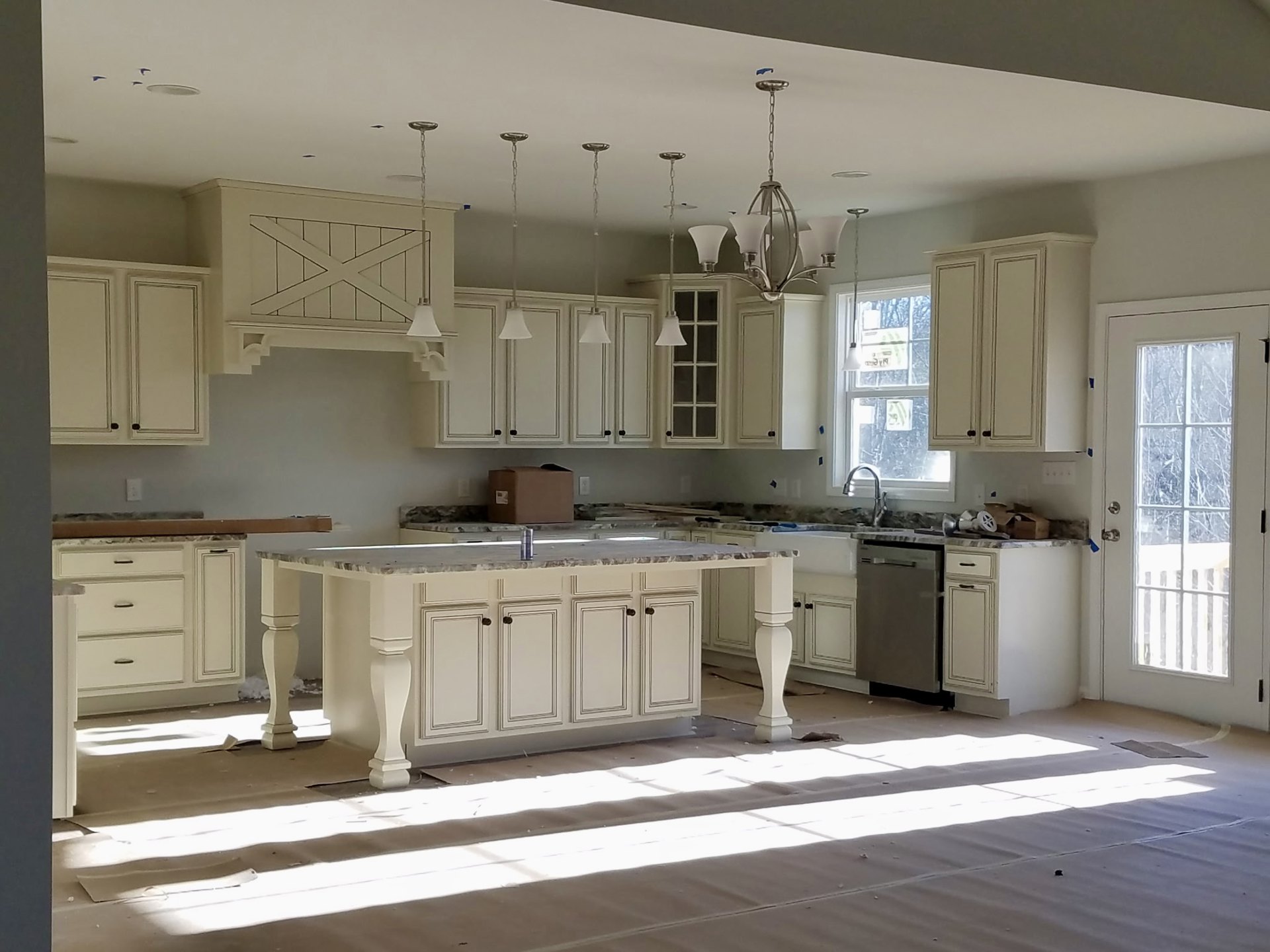 Spacious kitchen featuring a large central island with white countertop, built-in sink, and cabinetry; door with glass window, light-colored carpet flooring, and modern pendant