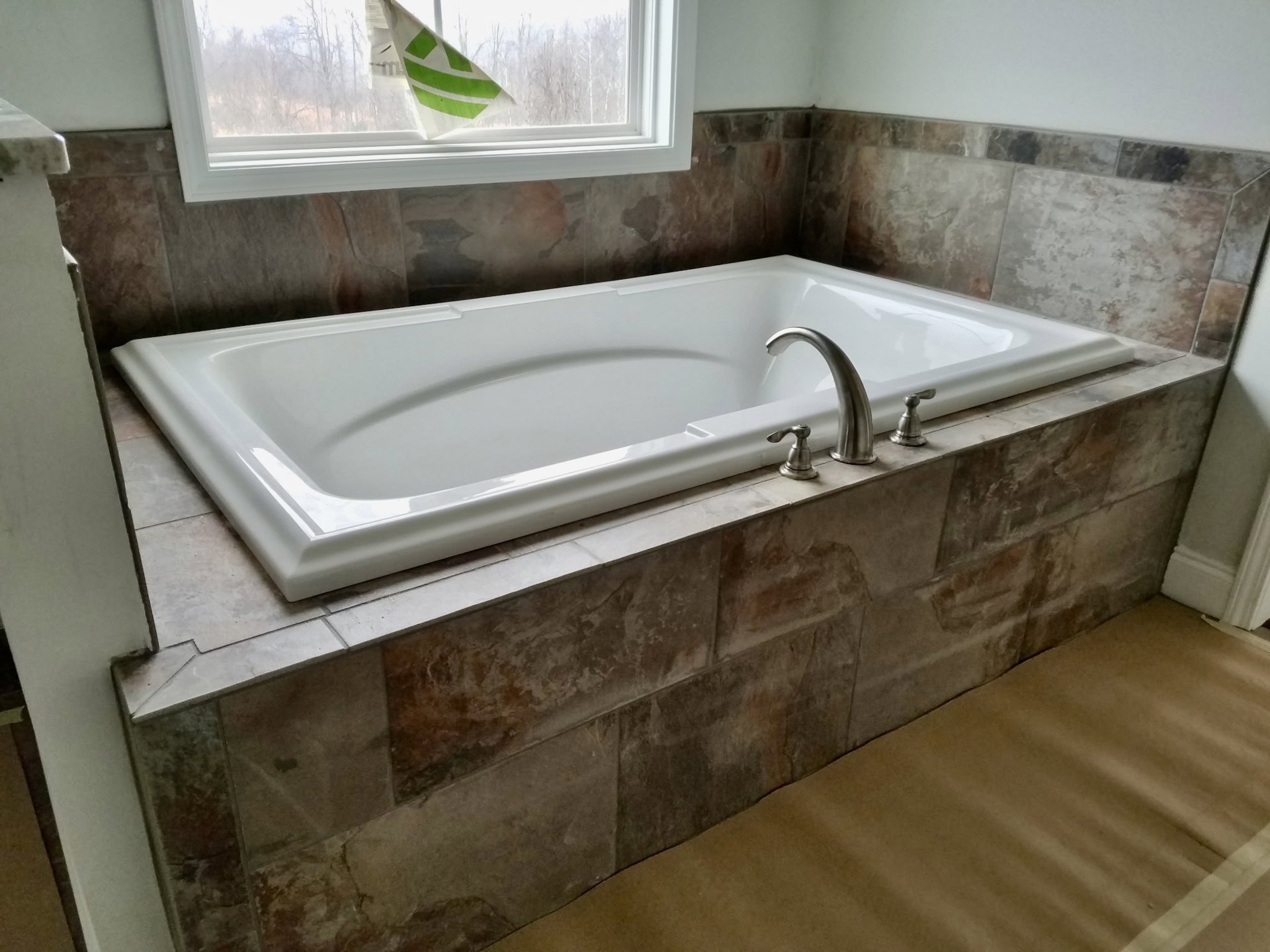 White freestanding bathtub with chrome faucet, white tile walls, window sill displaying green and white flag