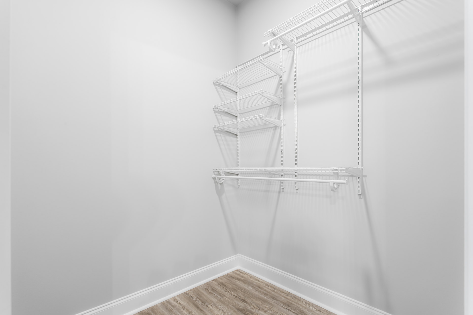 White built-in shelves with metal rods in an empty closet, wood flooring and white walls, overhead lighting.