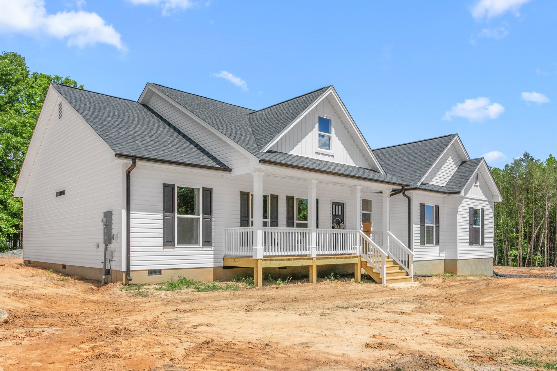 White house under construction with wooden porch and white framed windows, dirt field in foreground, Robert Frost Farm visible in background, cloudy sky overhead.