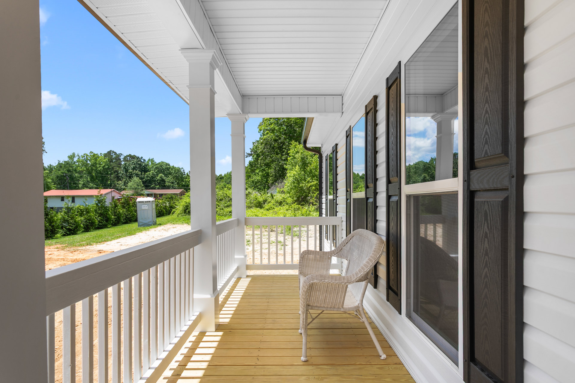 White porch with white railing, wooden bench, and wicker chair; windows and plants visible, outdoor setting.