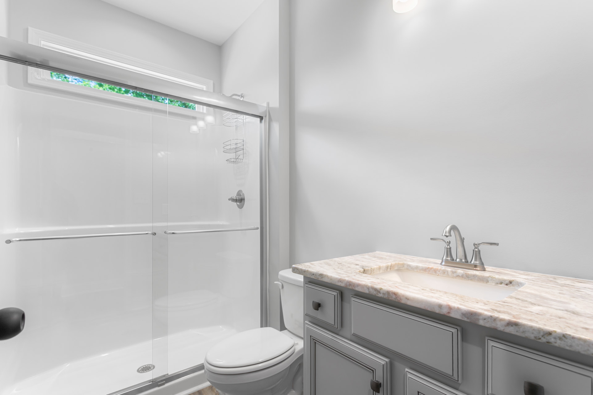 Bathroom with glass shower enclosure, white toilet, modern sink and faucet, light tile walls, and dark hardware accents