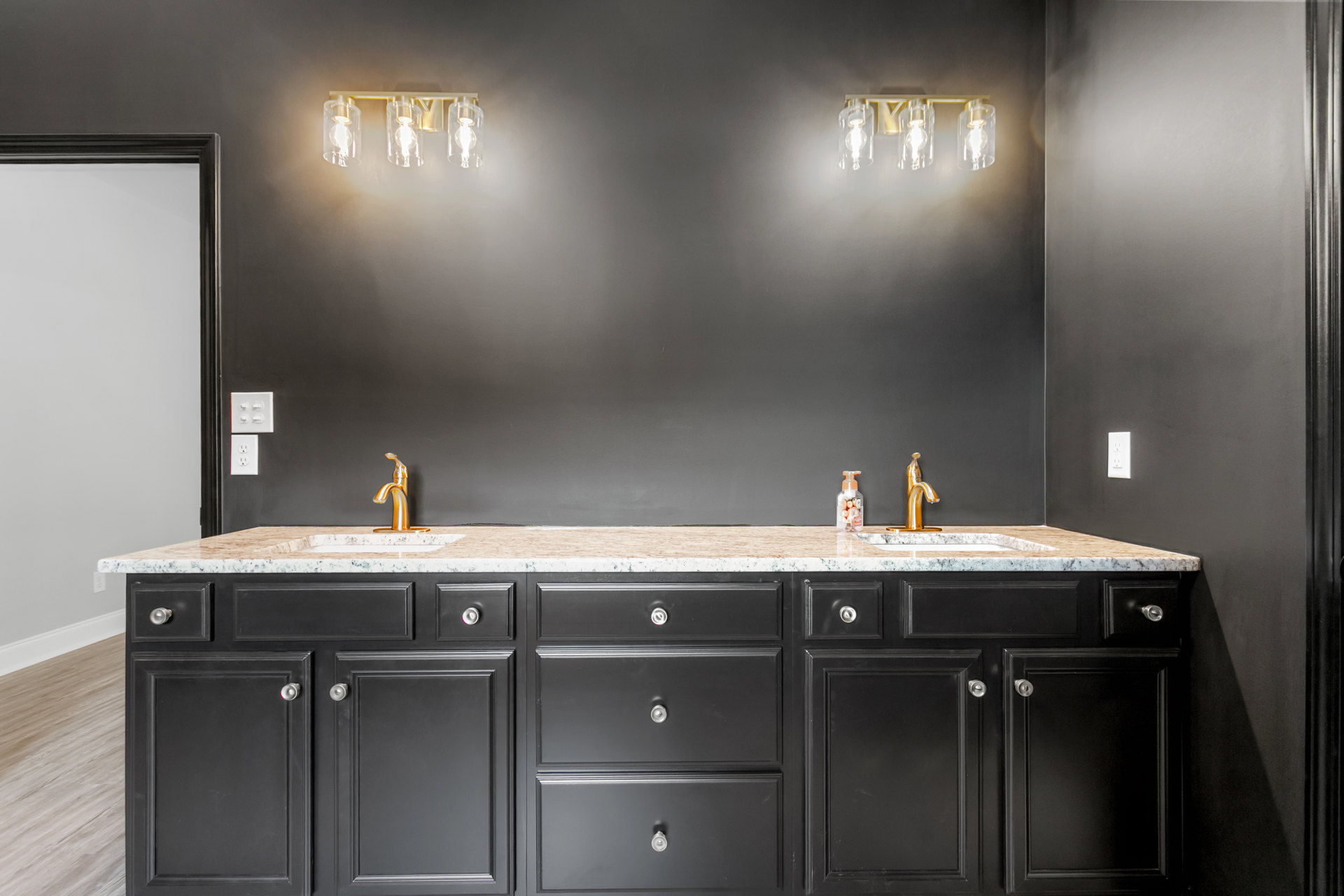 Bathroom featuring black cabinetry with silver knobs, marble countertops, dual sinks, chrome faucets, and white tile backsplash