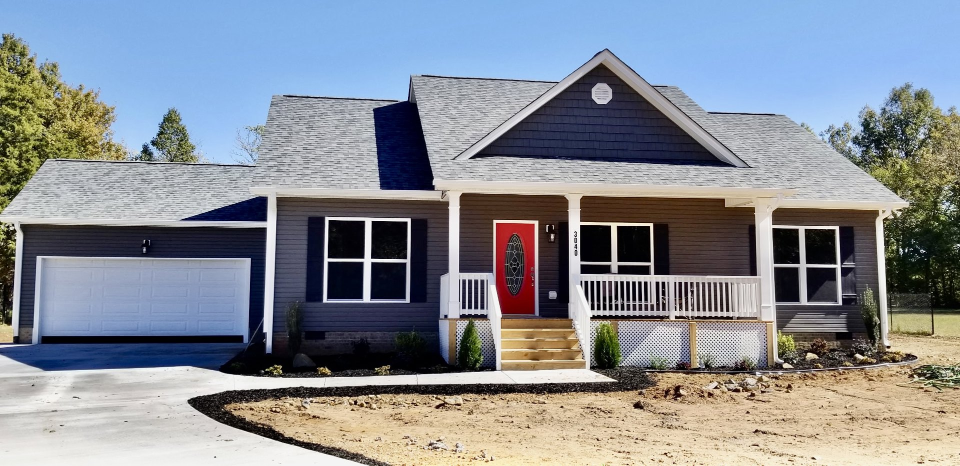 Blue siding exterior with white trim, red front door featuring oval window, white garage door with black trim, white-framed window, white vent, and potted green plant on porch