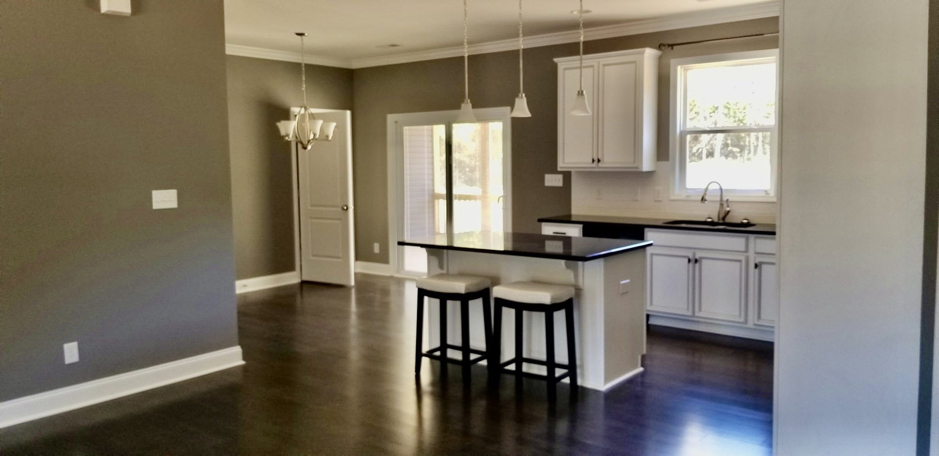 Modern kitchen with white cabinetry, light stone countertop bar, two stools with white cushions, stainless steel sink, window with white frame, and white door with silver handle
