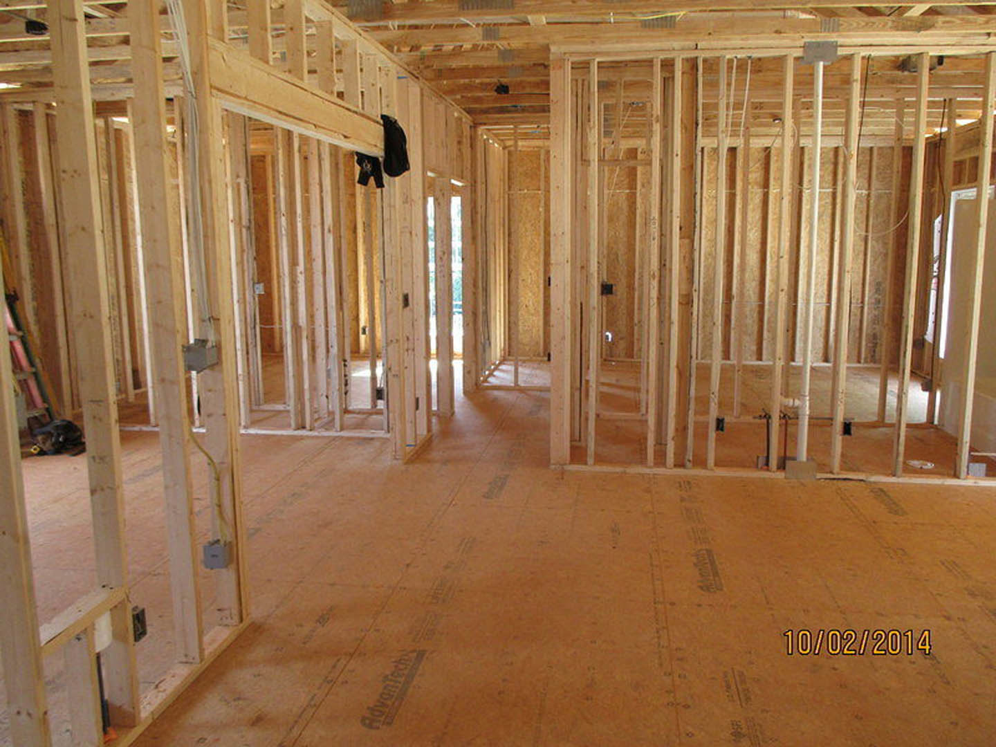 Room under construction with exposed wood framing, unfinished plank flooring, wooden ceiling beams, and insulation visible between studs; a black bird perched on a beam and a