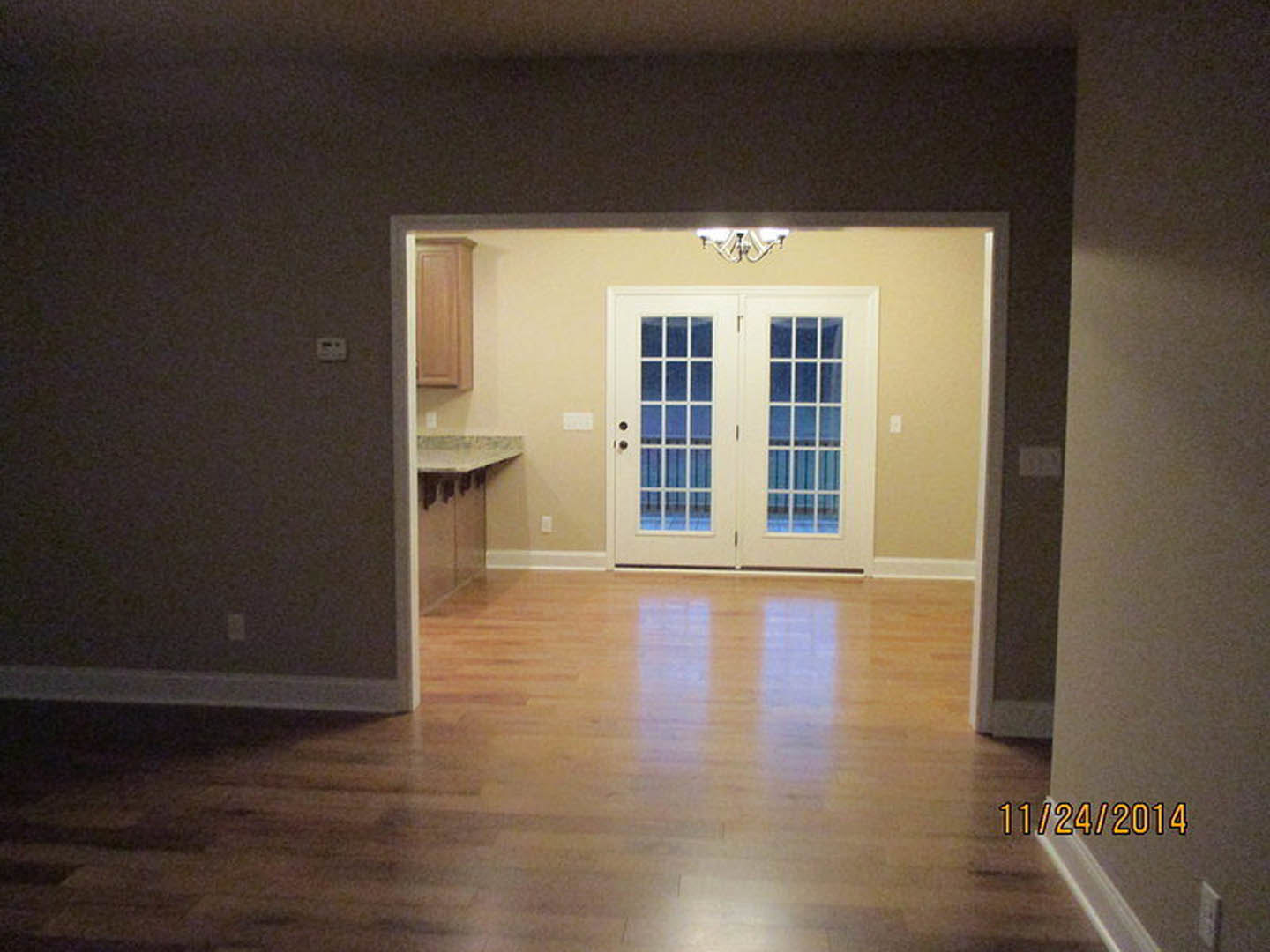 Dining room with hardwood flooring, double glass-paneled doors, wood wall paneling, and a wall-mounted light fixture