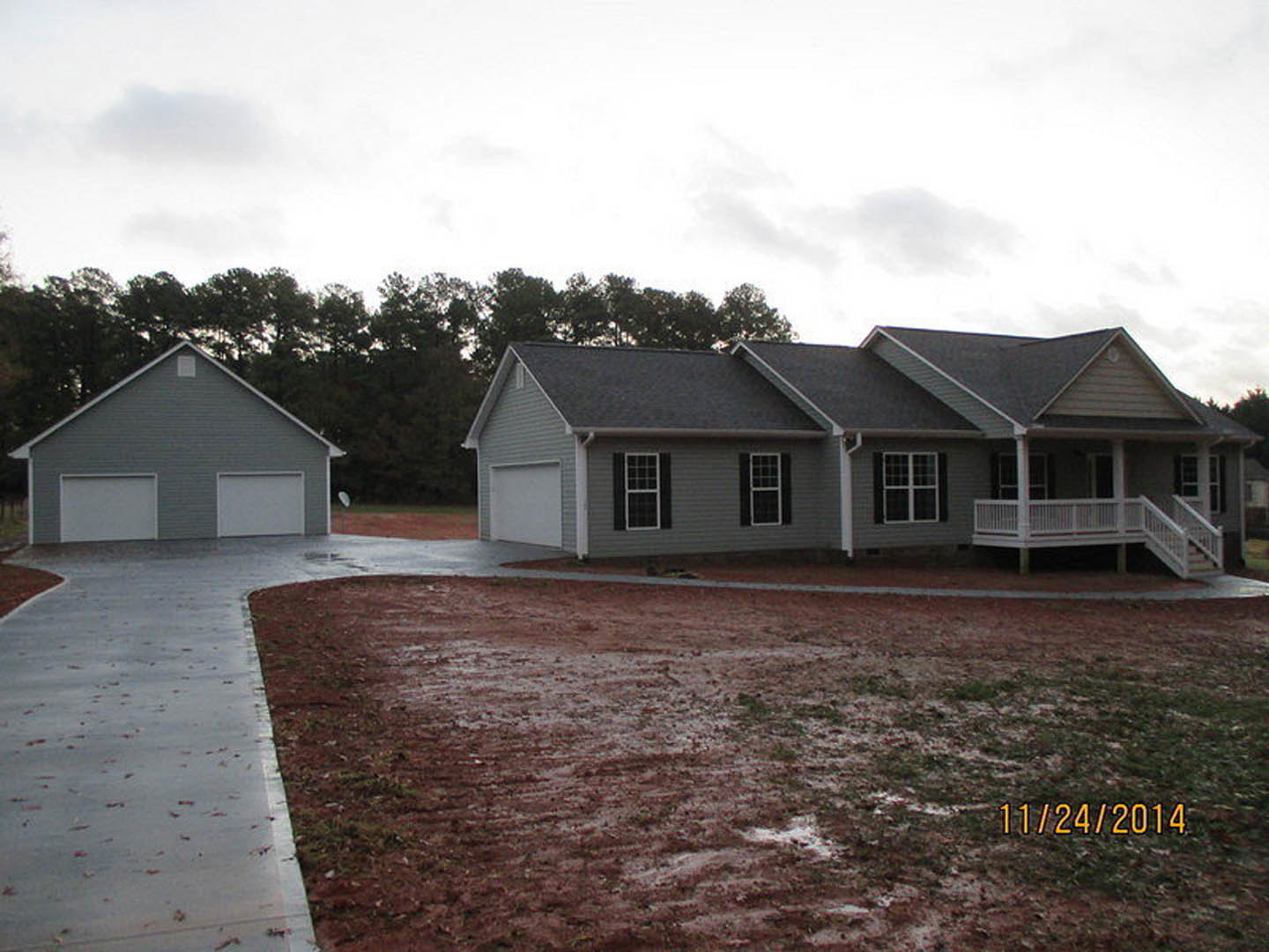 Two-story house with attached garage, paved driveway, white railings on front porch, gray roof with gutters, white-framed windows, and landscaped yard with trees under partly