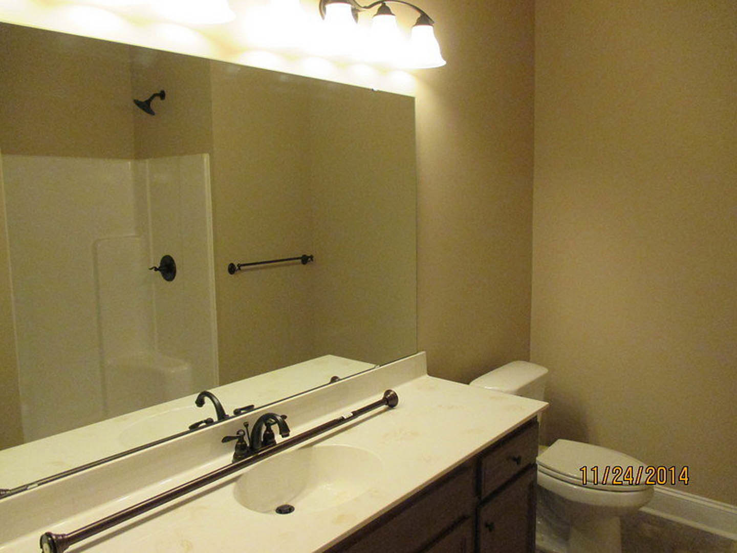 Bathroom with wide wall mirror above white countertop and sink, chrome faucet, open-lid toilet beside vanity, light tile flooring, and modern door handle in foreground